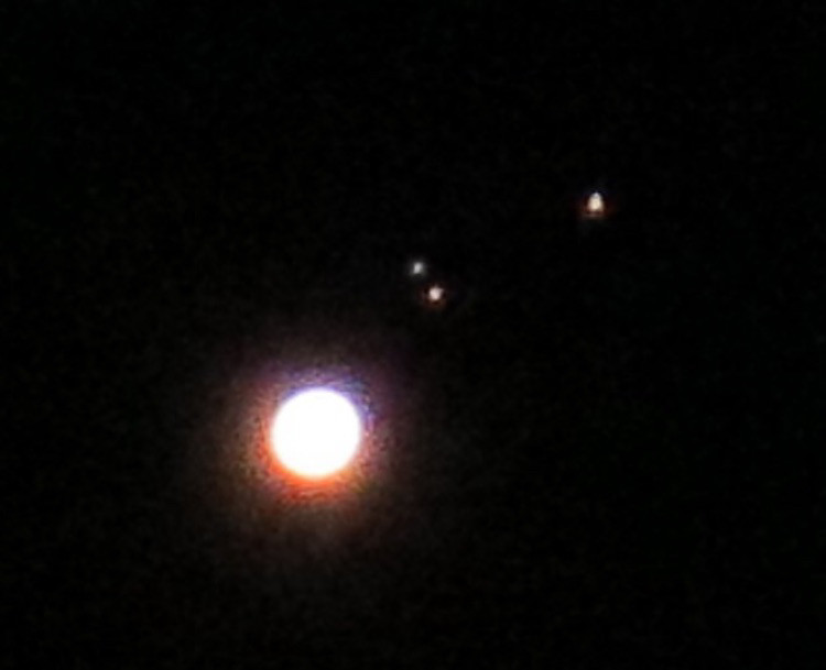 Photo of a big glowing sphere, Jupiter, with three visible smaller dots to its right