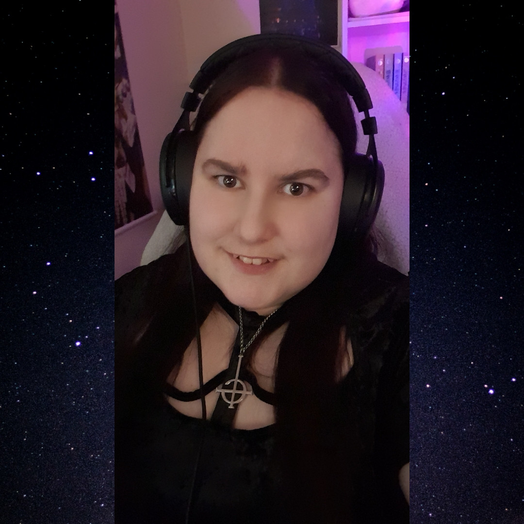 The picture features Cosmic smiling wearing black over-ear headphones. She is wearing a black dress with a spiderweb cut-out on the front at the neck. She has her hair straightened and is wearing a ghost necklace. The border of the picture is a black background with lots of stars on it