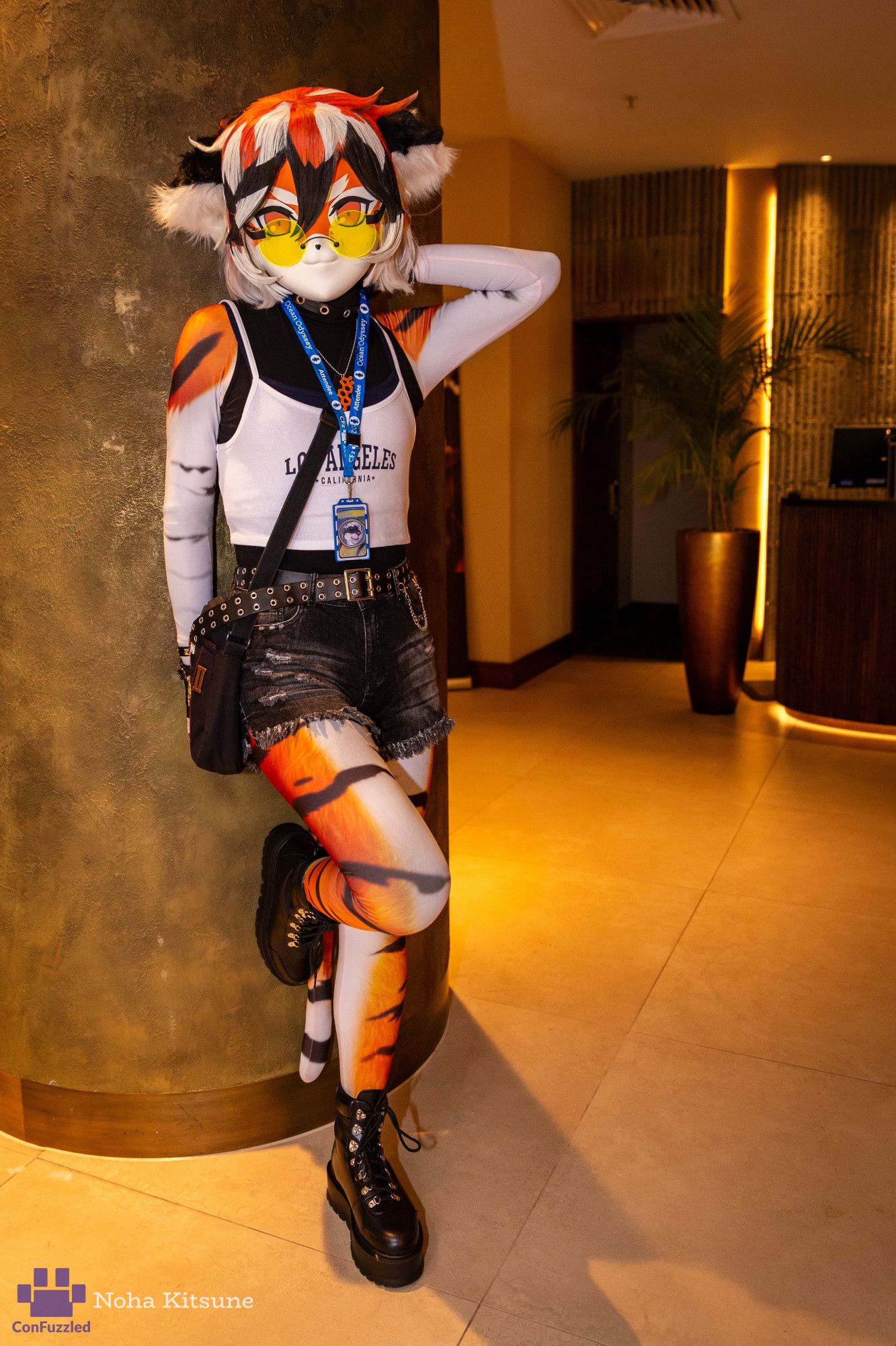 Photo of a kigurumi costume of the tiger girl Waai Fu, from the videogame Arknights. She is leaning against a pillar, touching the back of her neck with one hand, and with one leg against the wall, looking at the camera.