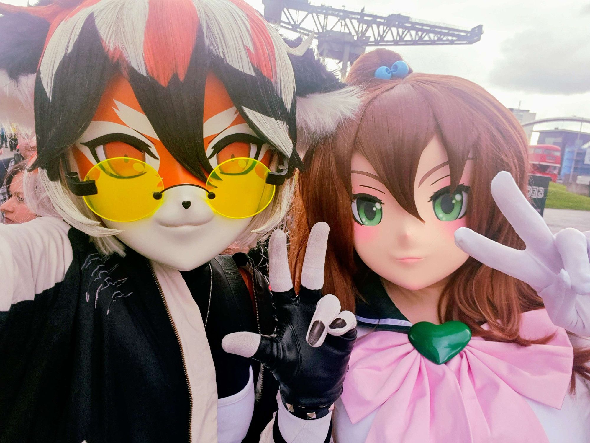 Kigurumi of the tiger girl Waai Fu from the videogame Arknights, and a kigurumi cosplaying Sailor Jupiter from Sailor Moon. They are both looking at the camera and making peace signs.