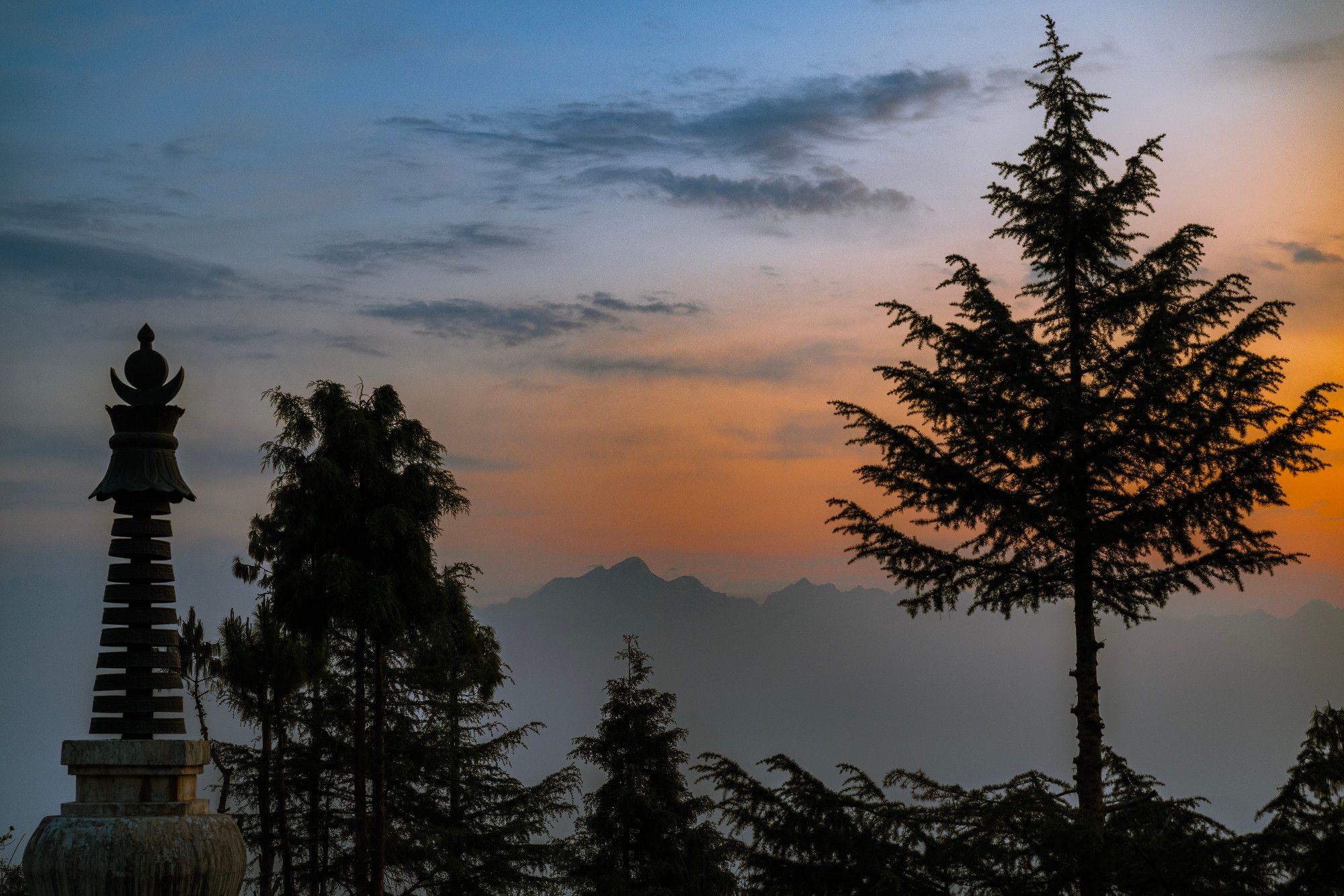 Silhouette of trees and Stupa at sunrise in an orange to blue gradient sky over Himalayan peaks in the background at The Fort Resort, Nagarkot, Nepal
Captured by Komeil Karimi