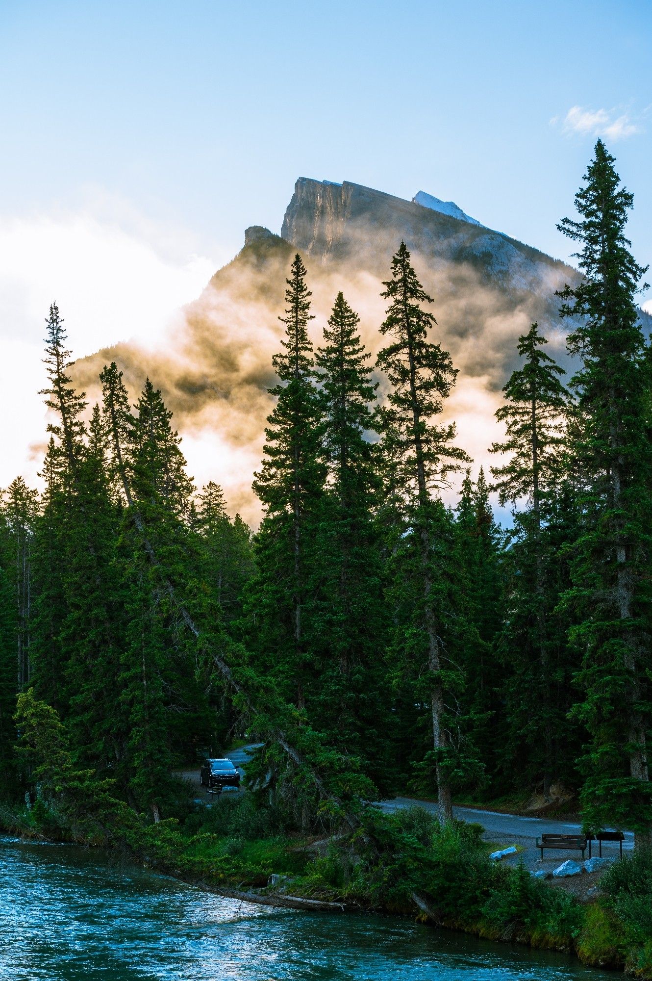 Fog covered Mount Rundle hit with early morning sunlight towering over Bow River with tall Rockies pine trees in city of Banff, Banff National Park, Alberta, Canada 
Captured by Komeil Karimi