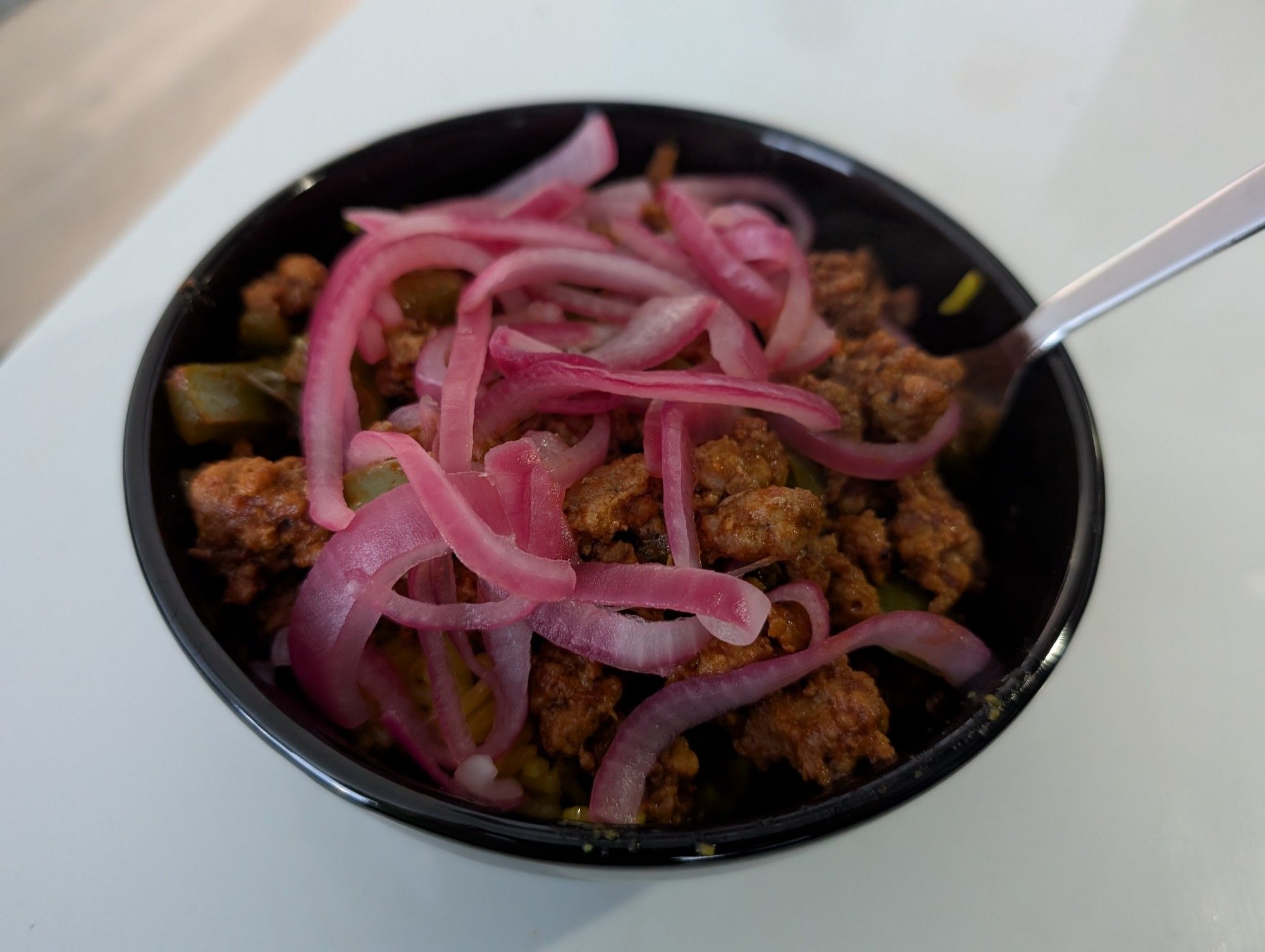 A black bowl with visible pork and red onions