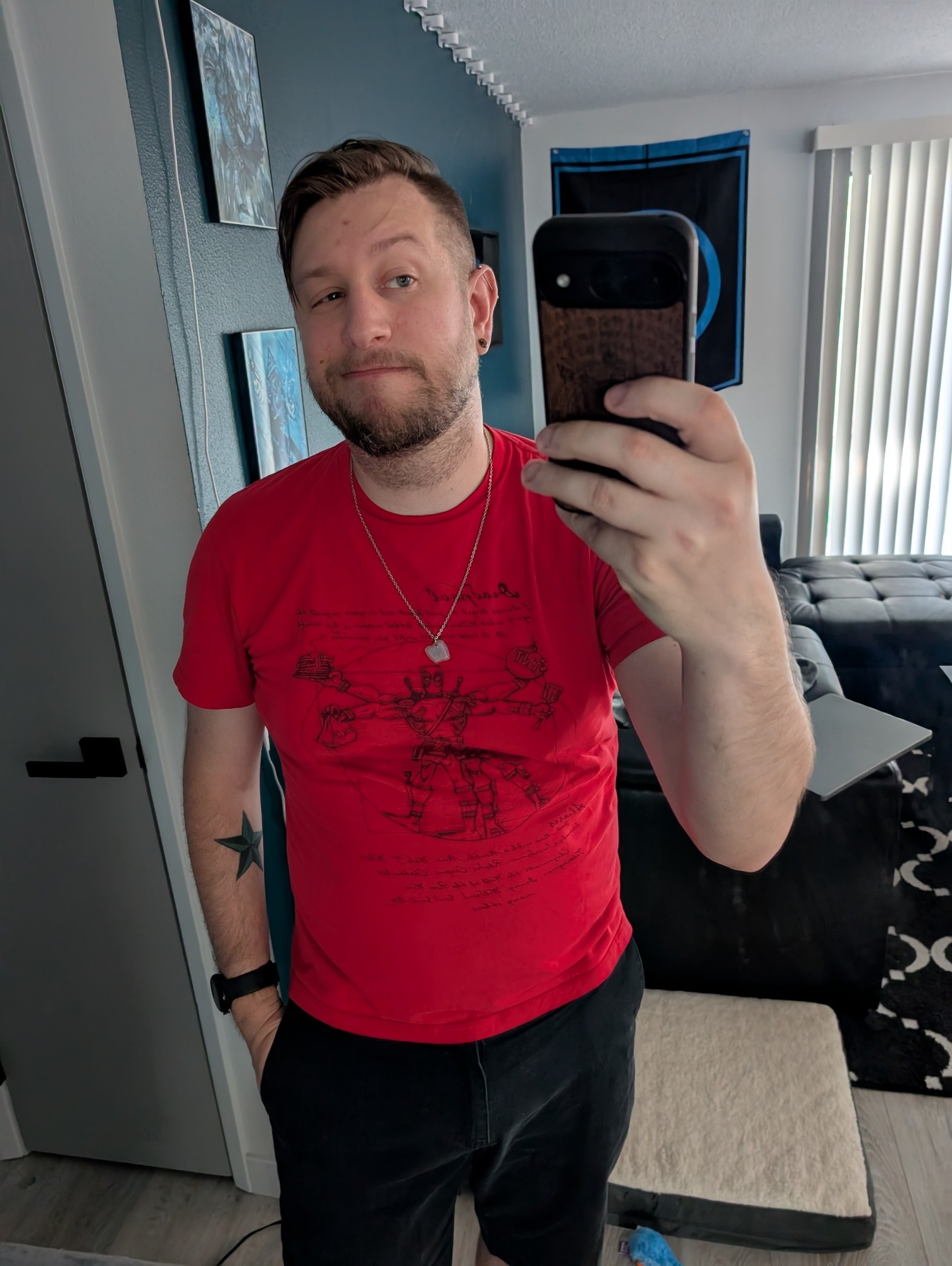 Standing in my living room with a smirk, wearing a red Deadpool+Vitruvian Man shirt and black shorts, sweaty as hell.