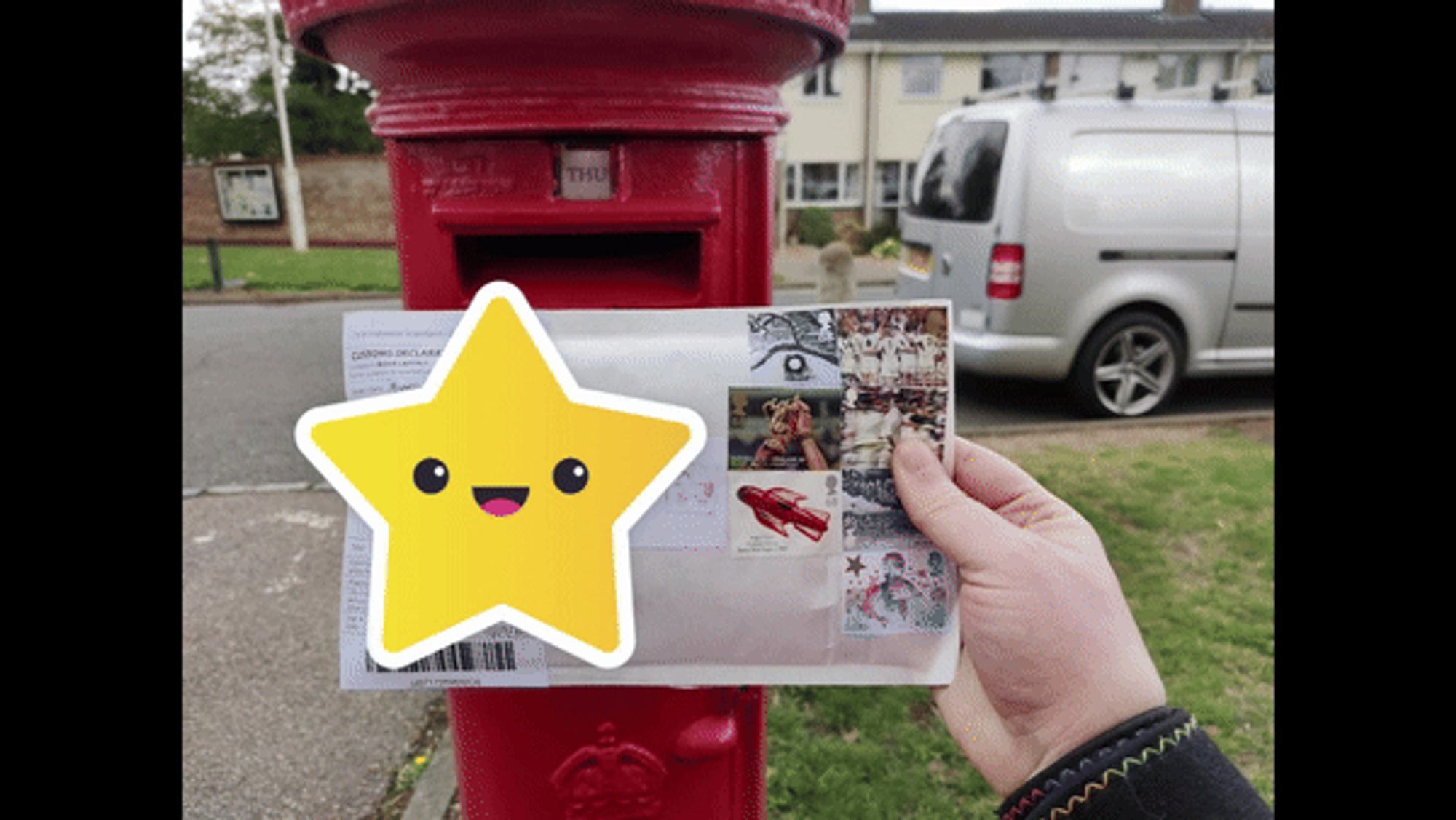 A hand holding up an mailer envelope in front of a red postbox. There is a dancing star covering the addresses.