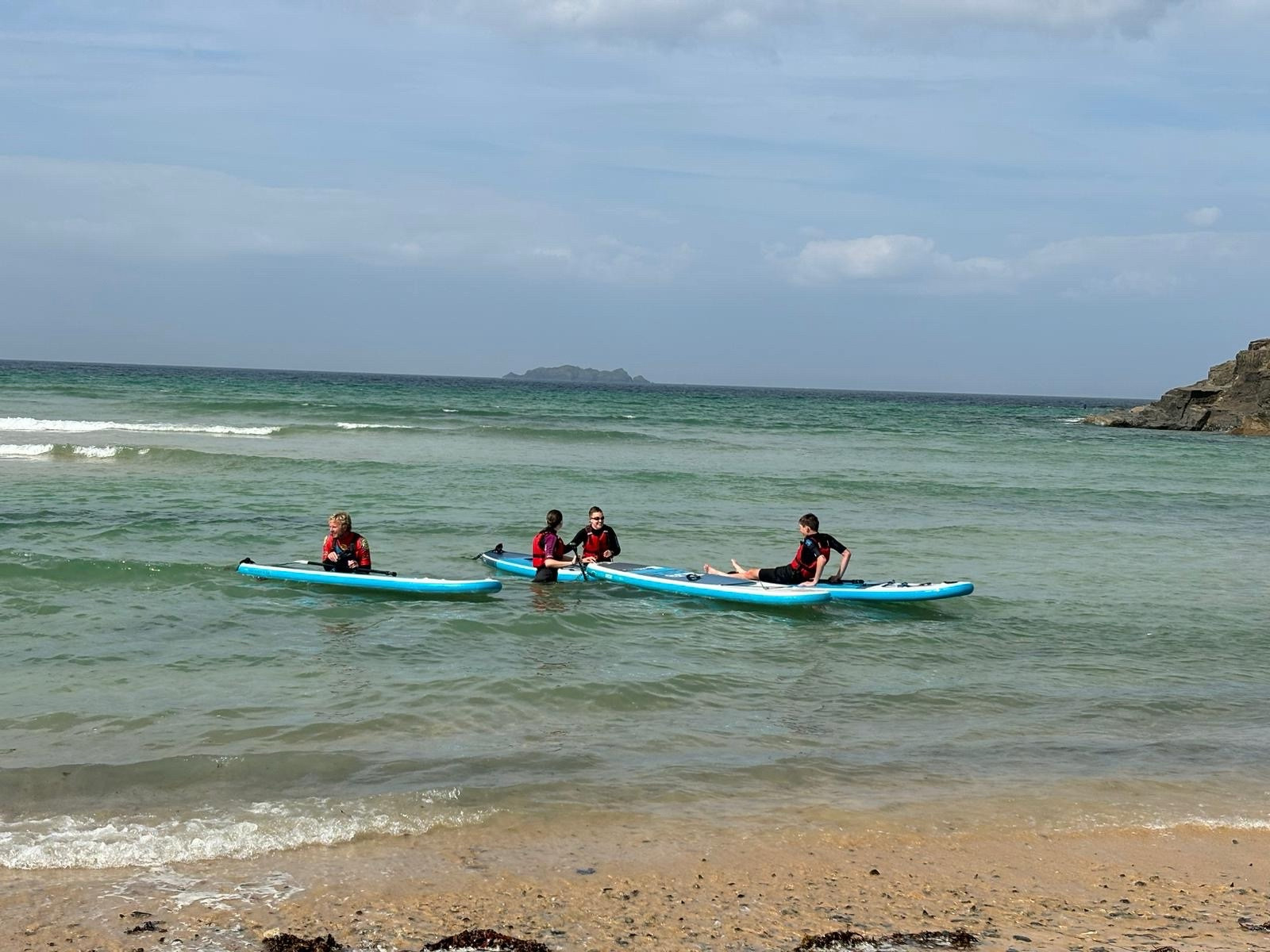 Photo of Emily and two teenagers in the sea with paddleboards.