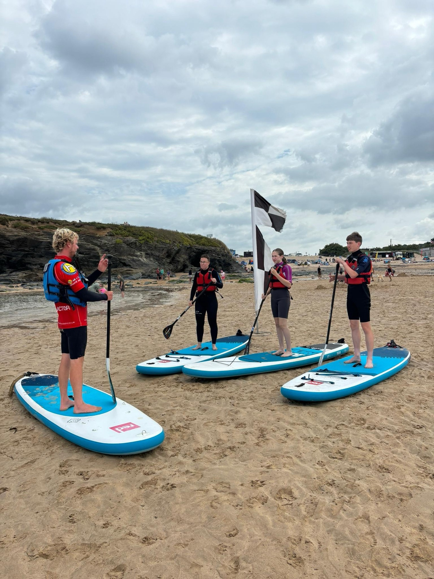 Photo of Emily and two teenagers standing on paddleboards on the beach being instructed.