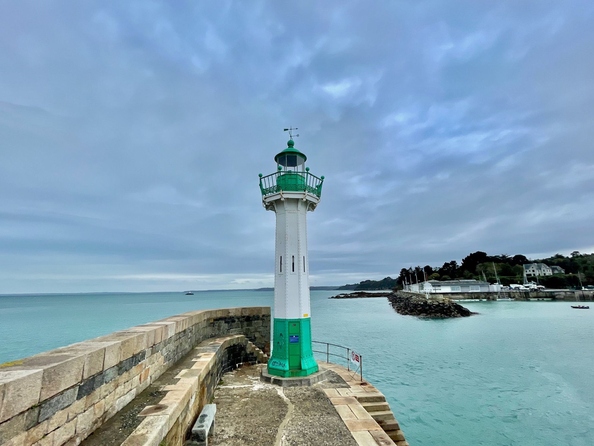 phare métallique blanc et vert au bout d'une jetée face à la mer de couleur verte et au ciel de couleur bleue