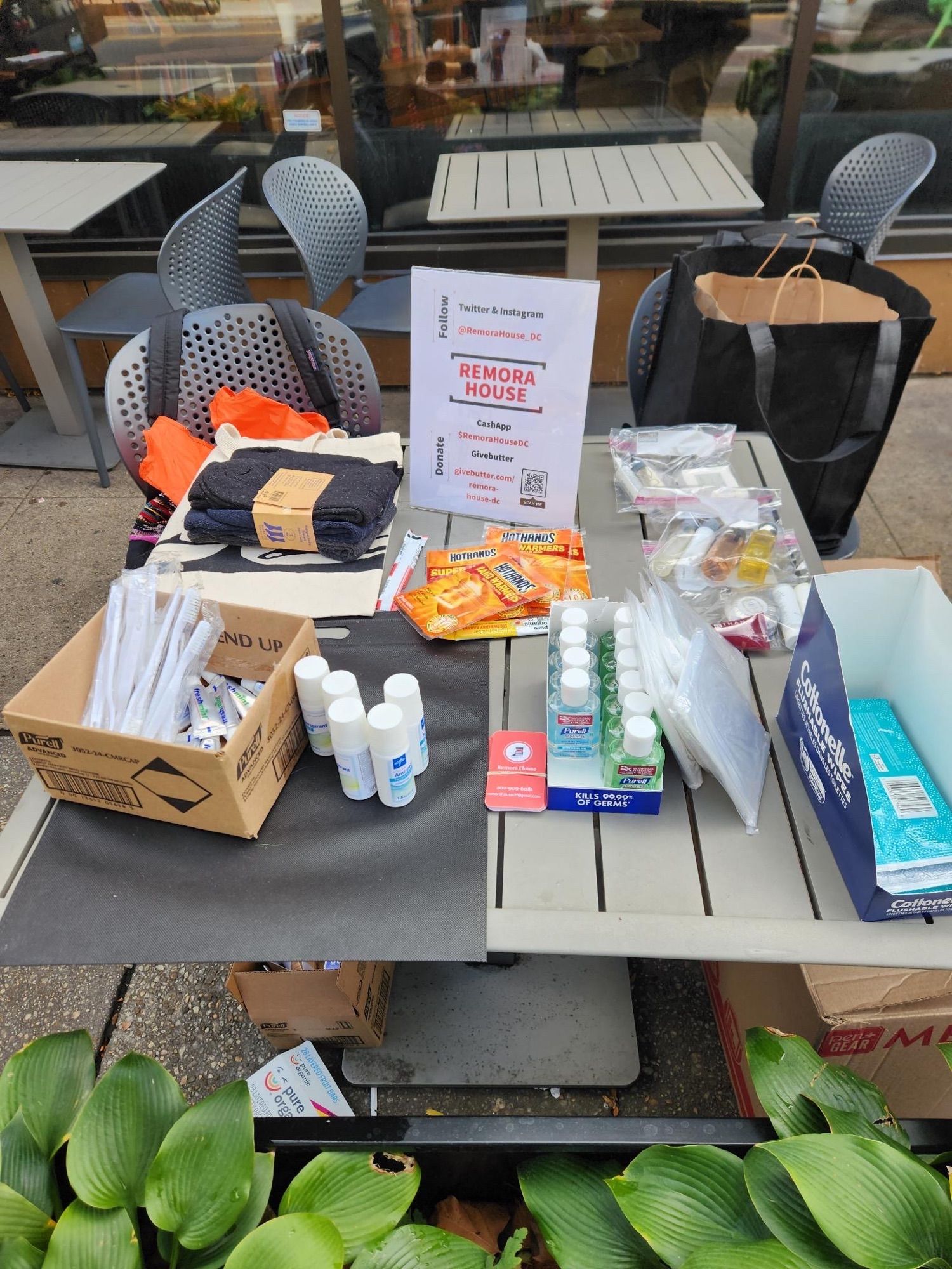 A small dining table on the sidewalk in front of potters house is covered in hygiene supplies, socks, and hand warmers for neighbors to take for free