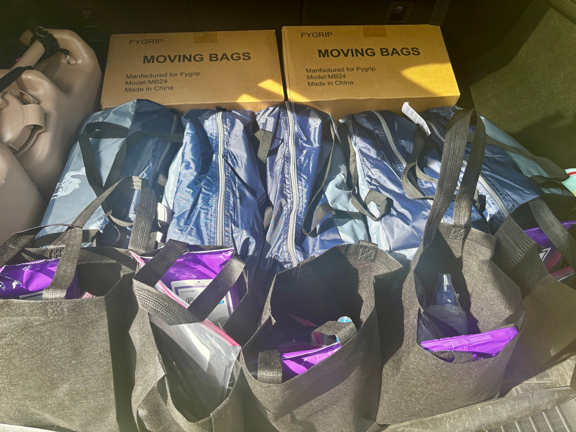 An open hatchback trunk with two boxes of moving bags, five tents, and five small black bags with camping supplies 