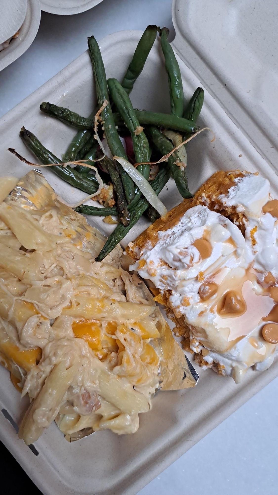 A to go box with green beans, a serving of chicken penne pasta, and a slice of pumpkin cake topped with whipped cream and butterscotch chips