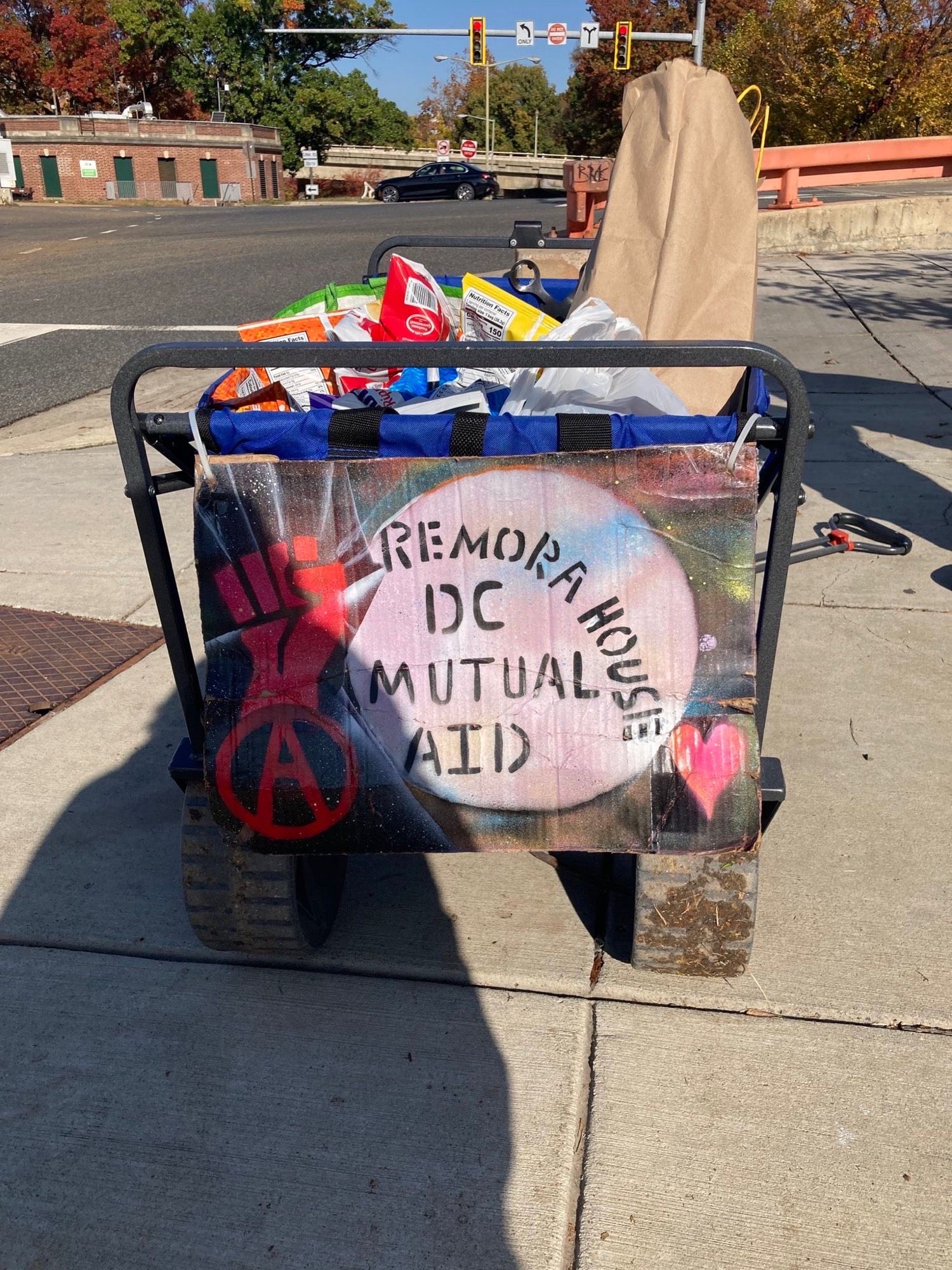 A cart with a hand painted remora house dc mutual aid sign on the front is filled with snacks and other supplies to hand out in camps in foggy bottom