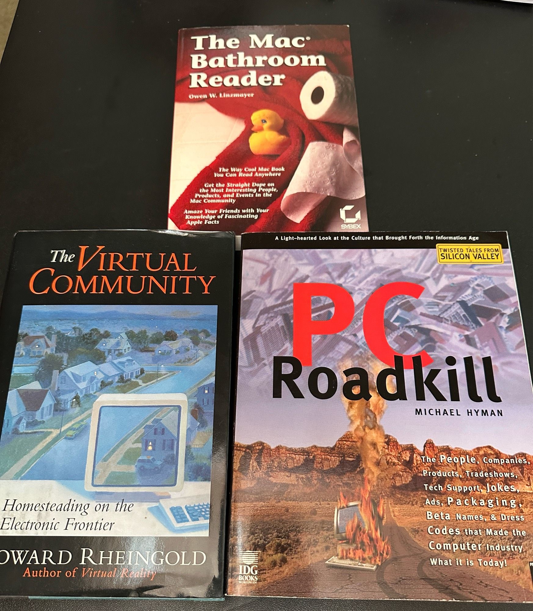 Three books: The Mac Bathroom Reader by Owen W. Linzmayer, The Virtual Community by Howard Rheingold, and PC Roadkill by Michael Hyman.