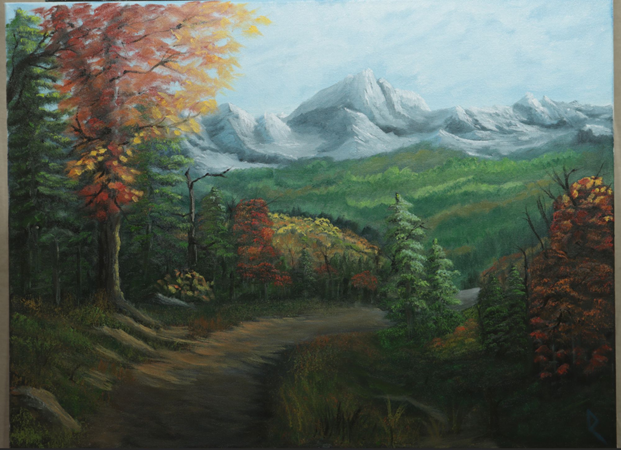 Oil painting of a mountain valley in autumn on 18"x24" canvas. A mountain range in the distance overlooks a dense, forested valley. A path of trees, rocks and grass leads toward the valley. Sunlight creates dynamic highlights amongst the mountains, forests and leaves.