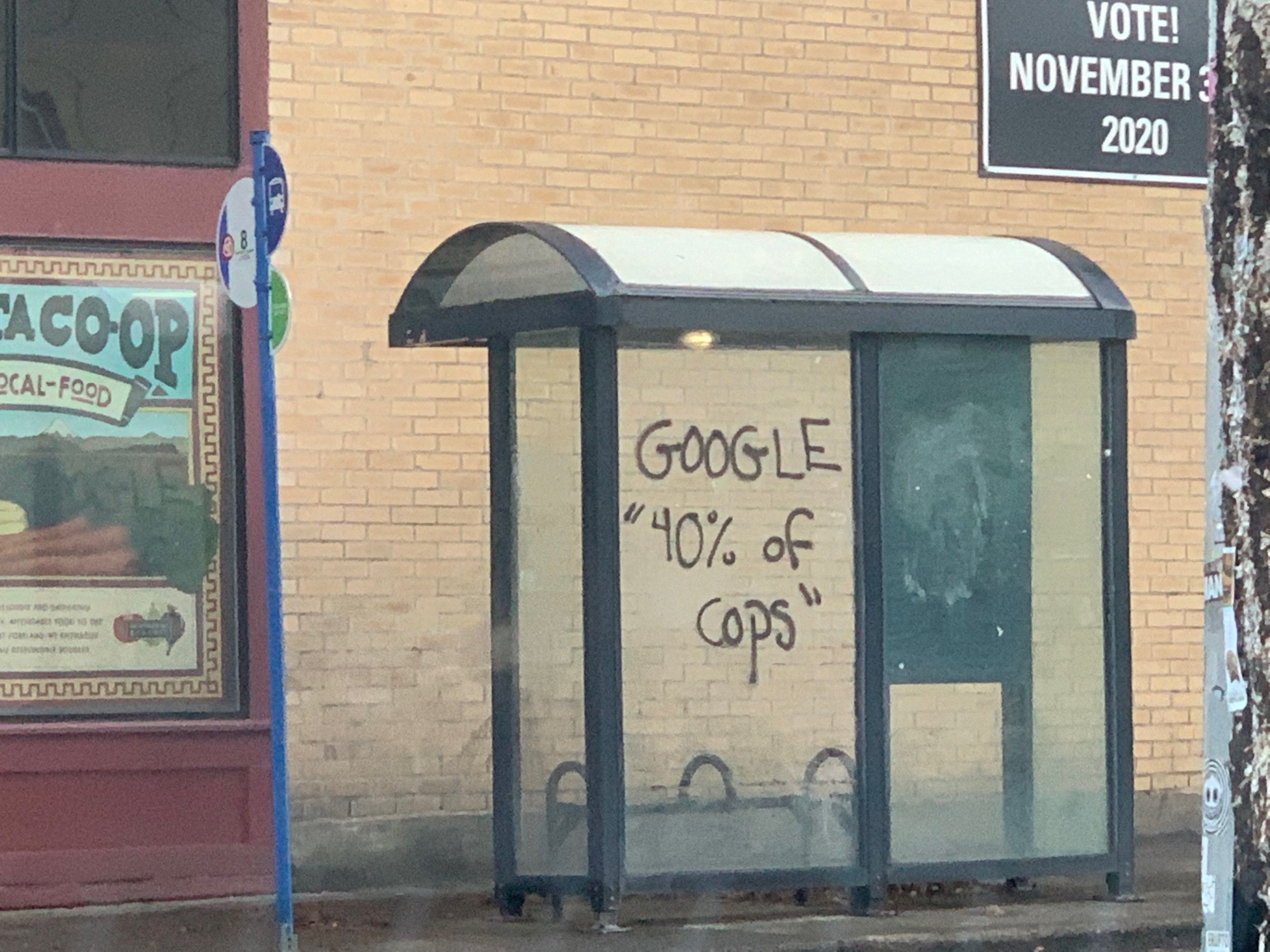 An image of a bus stop and the glass has graffiti on it that says “GOOGLE ‘40% of cops’”