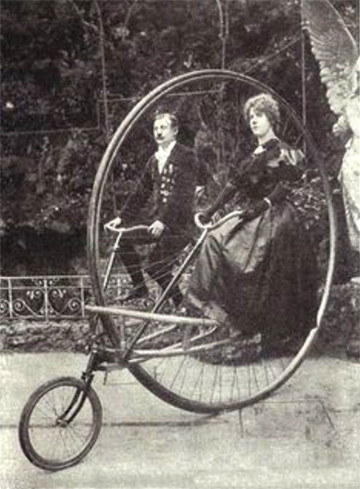 black and white photo of a Penny Farthing bicycle, BUT..picture the bike the other way round, so the smaller wheel is at the front. now imagine there is no seat at the top, instead two seats - one each side of the giant main wheel, with pedals under each. a very smartly dressed couple sit in the seats, holding handlebars with a long shaft that goes down to the front wheel