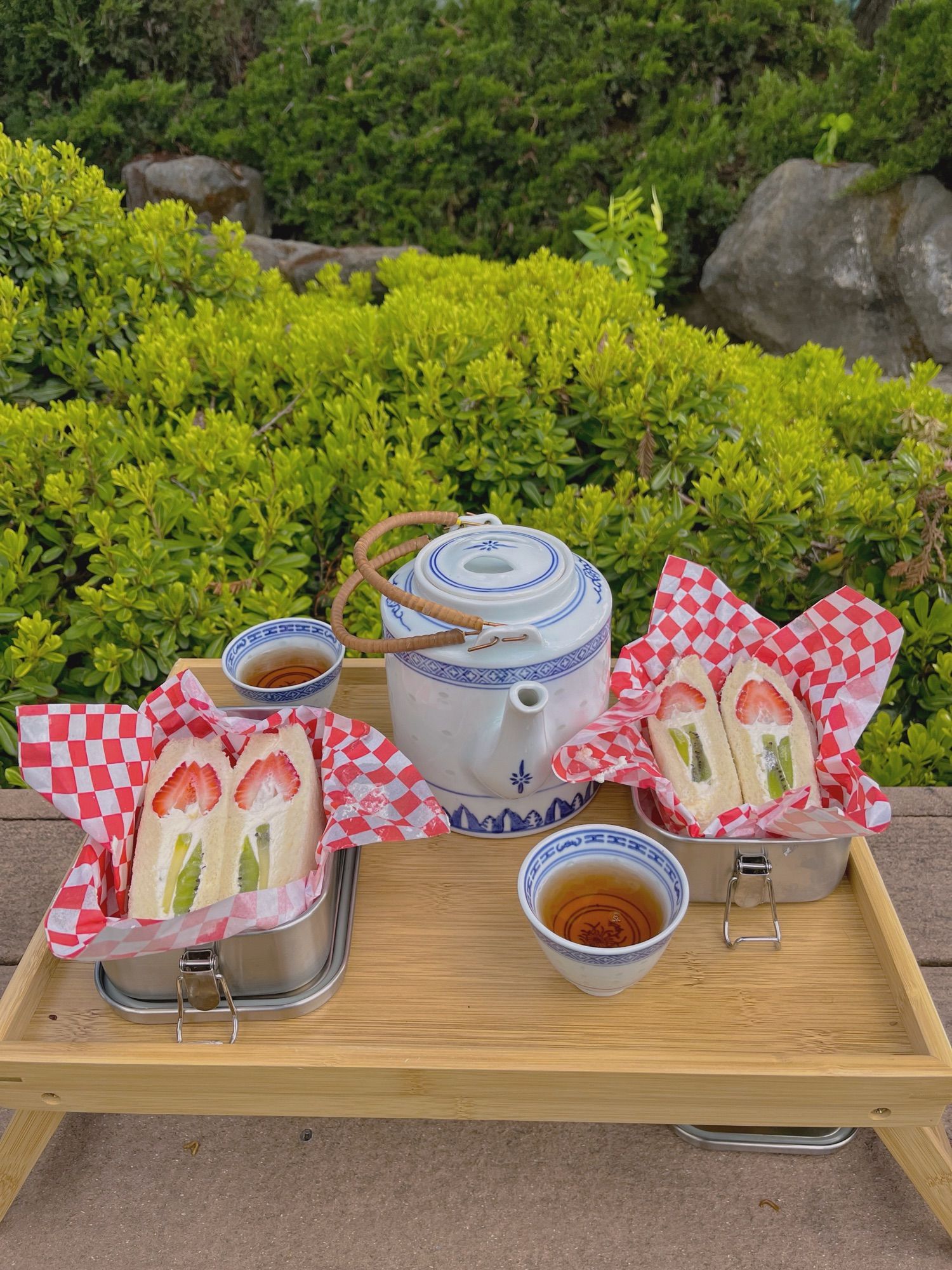 a tea tray with tulip fruit sandwiches, a teapot, and two tea cups