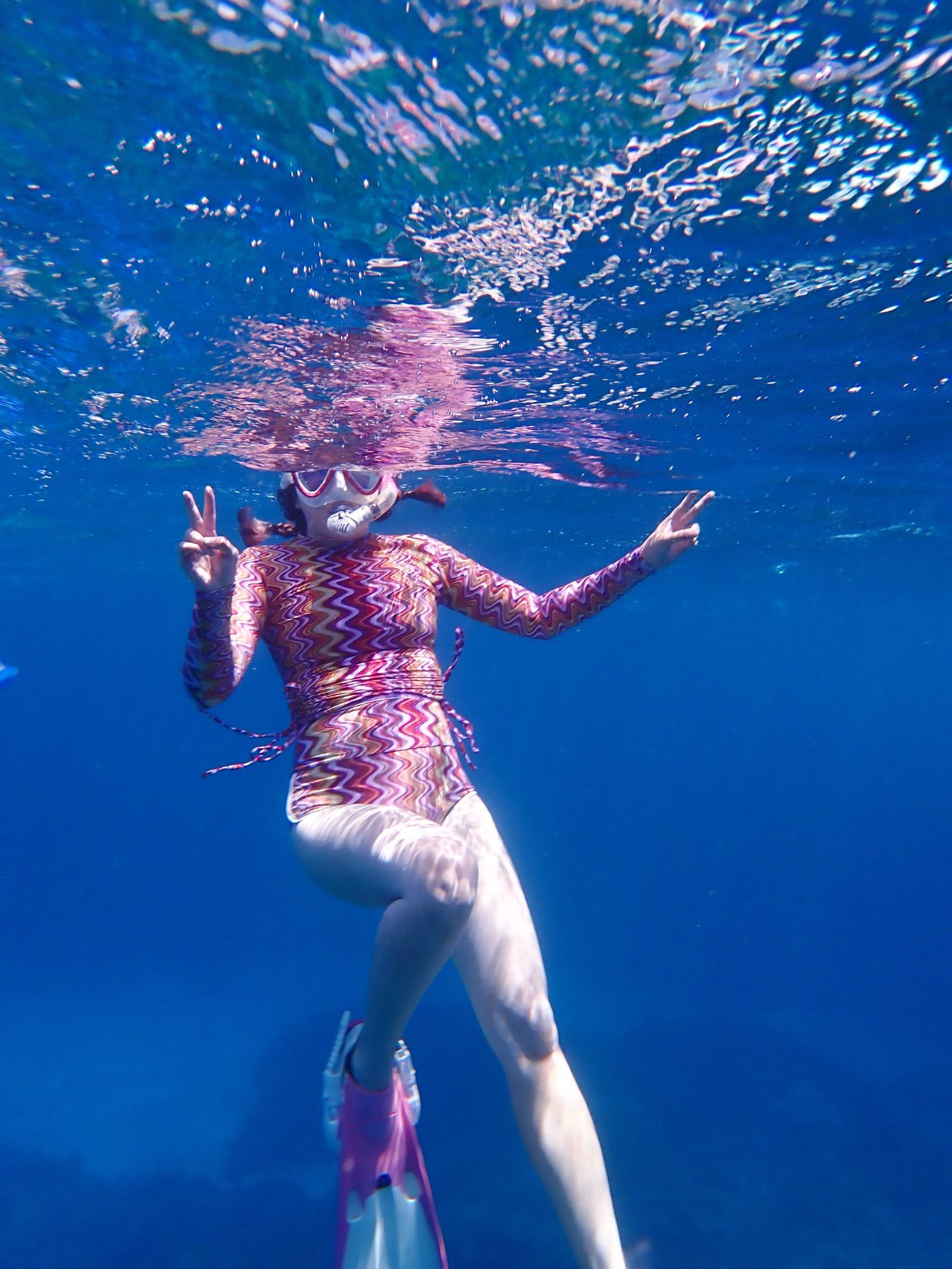 me wearing a patterned pink, brown, and purple wetsuit snorkeling in the ocean