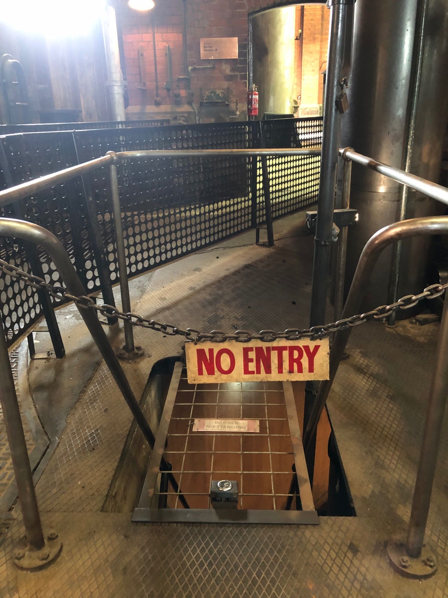 A “no entry” sign hanging from chain links in front of a narrow staircase inside an industrial room.