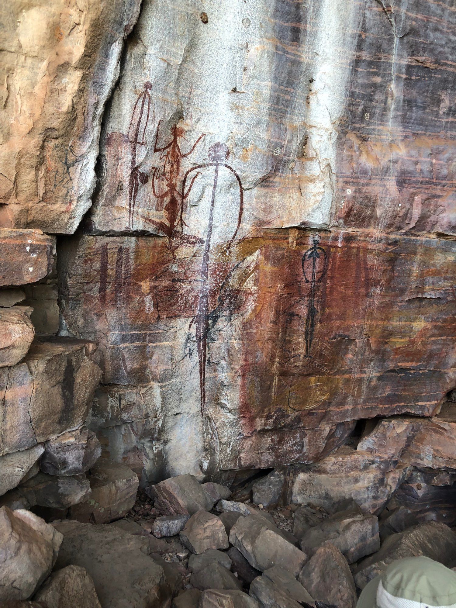 Striated rock face with human figures and other things drawn.