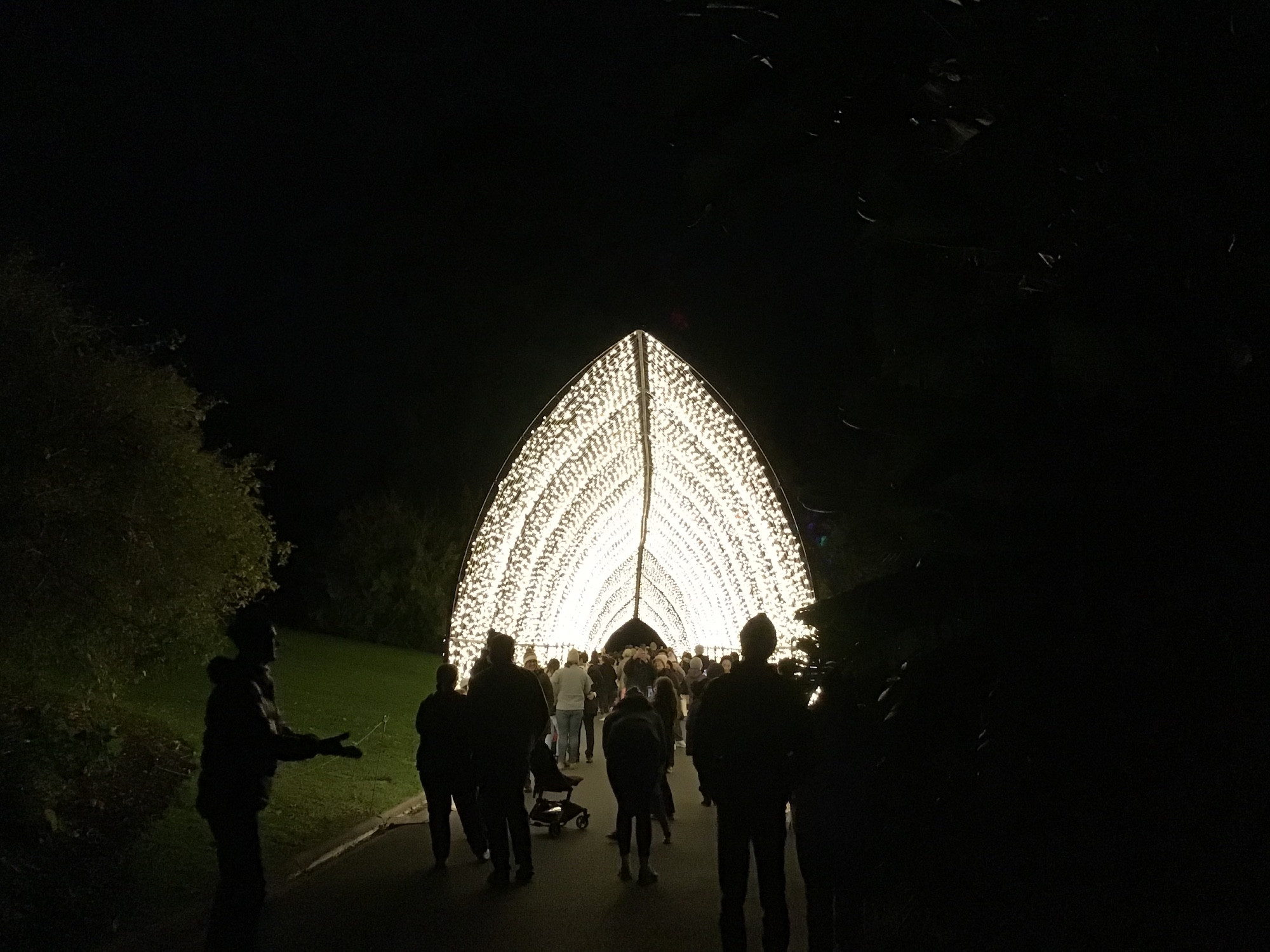 An arched tunnel of white lights shining in the darkness with people silhouetted as they enter