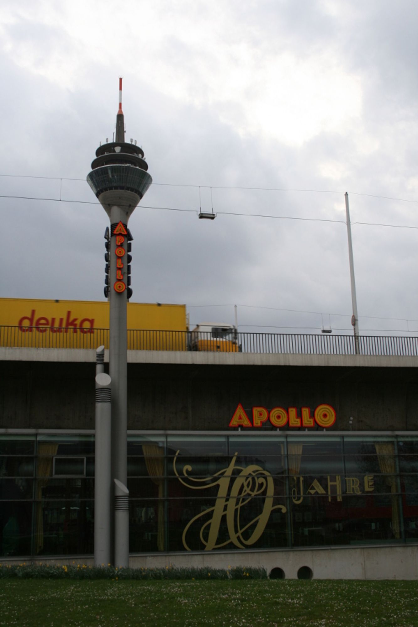 Düsseldorf, Rheinkniebrücke, Apollo Varieté, der Rheinturm scheint aus einer der Säulen der Apollo-Leuchtreklame herauszuragen. Ein auf der Brücke fahrender LKW verstärkt die optische Täuschung indem er den etwas dickeren Rheinturm verdeckt.