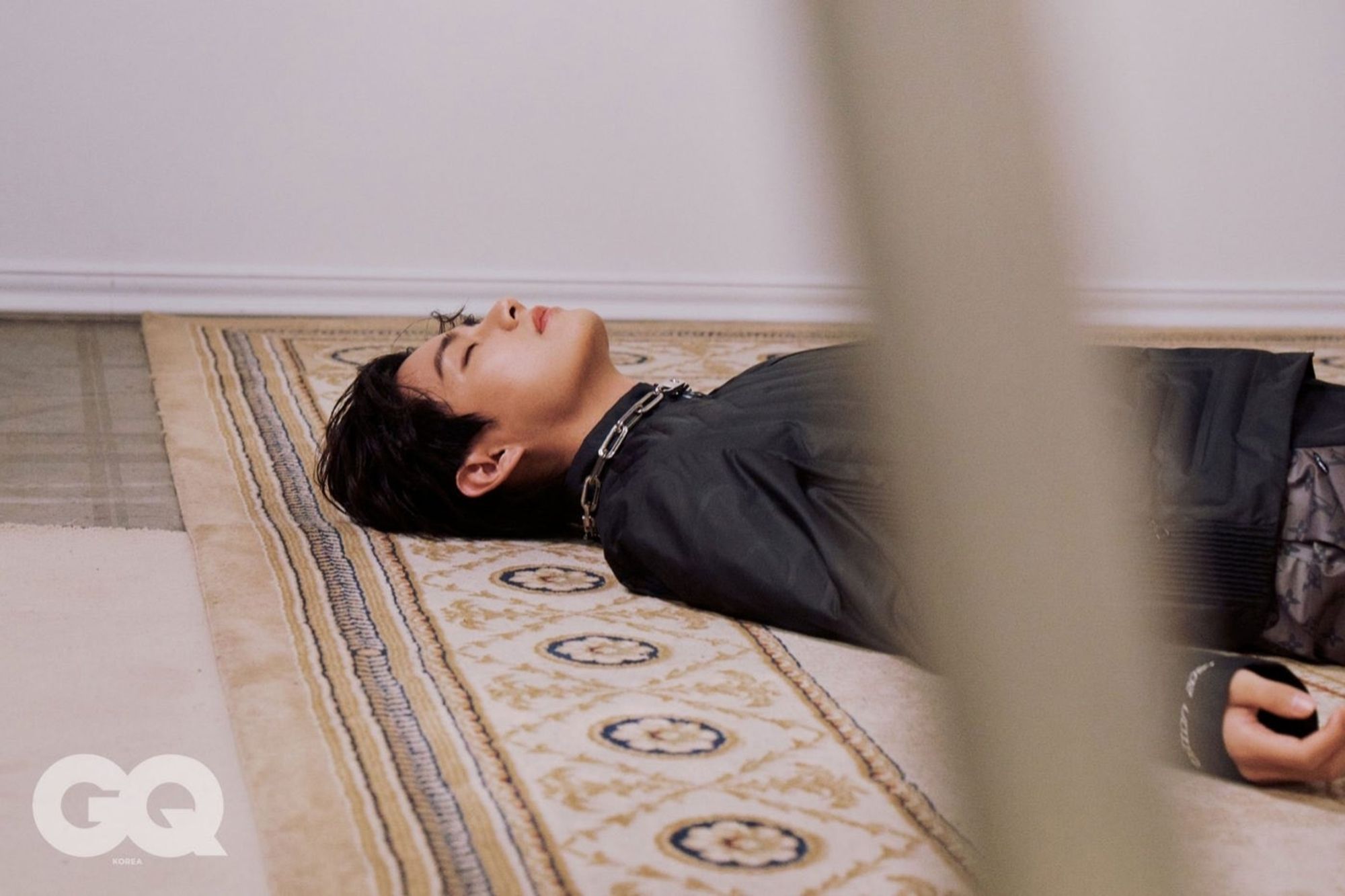 Taehyung in black laying on a rug. GQ photoshoot