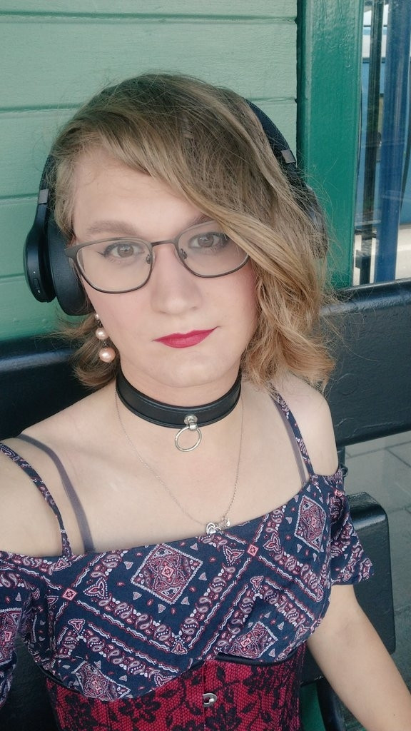 Girl wearing a black collar and a black and red patterned dress sitting and waiting at a train station 