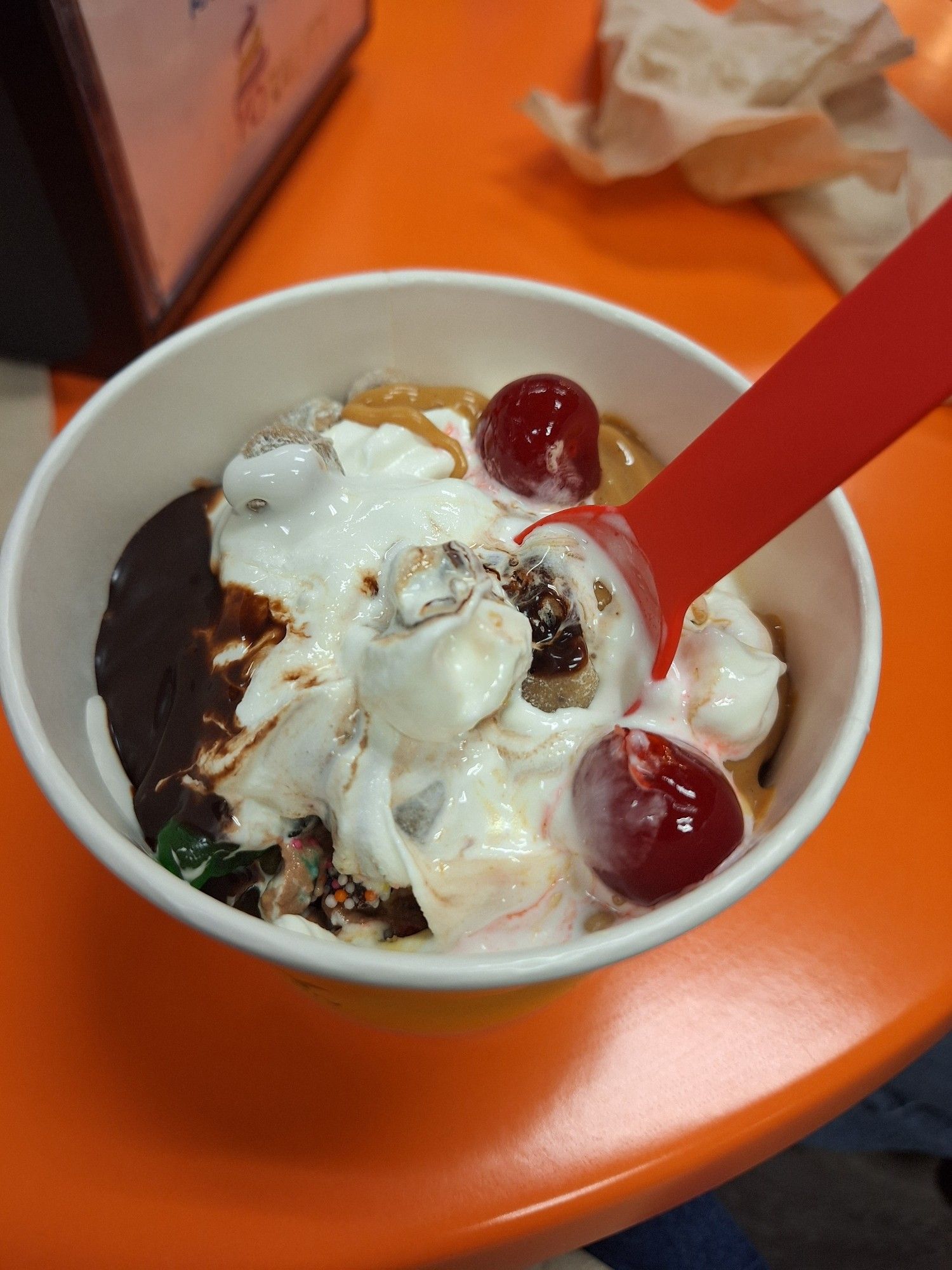 A big bowl of frozen yogurt with a bunch of candy, sauces, and cherries on top.