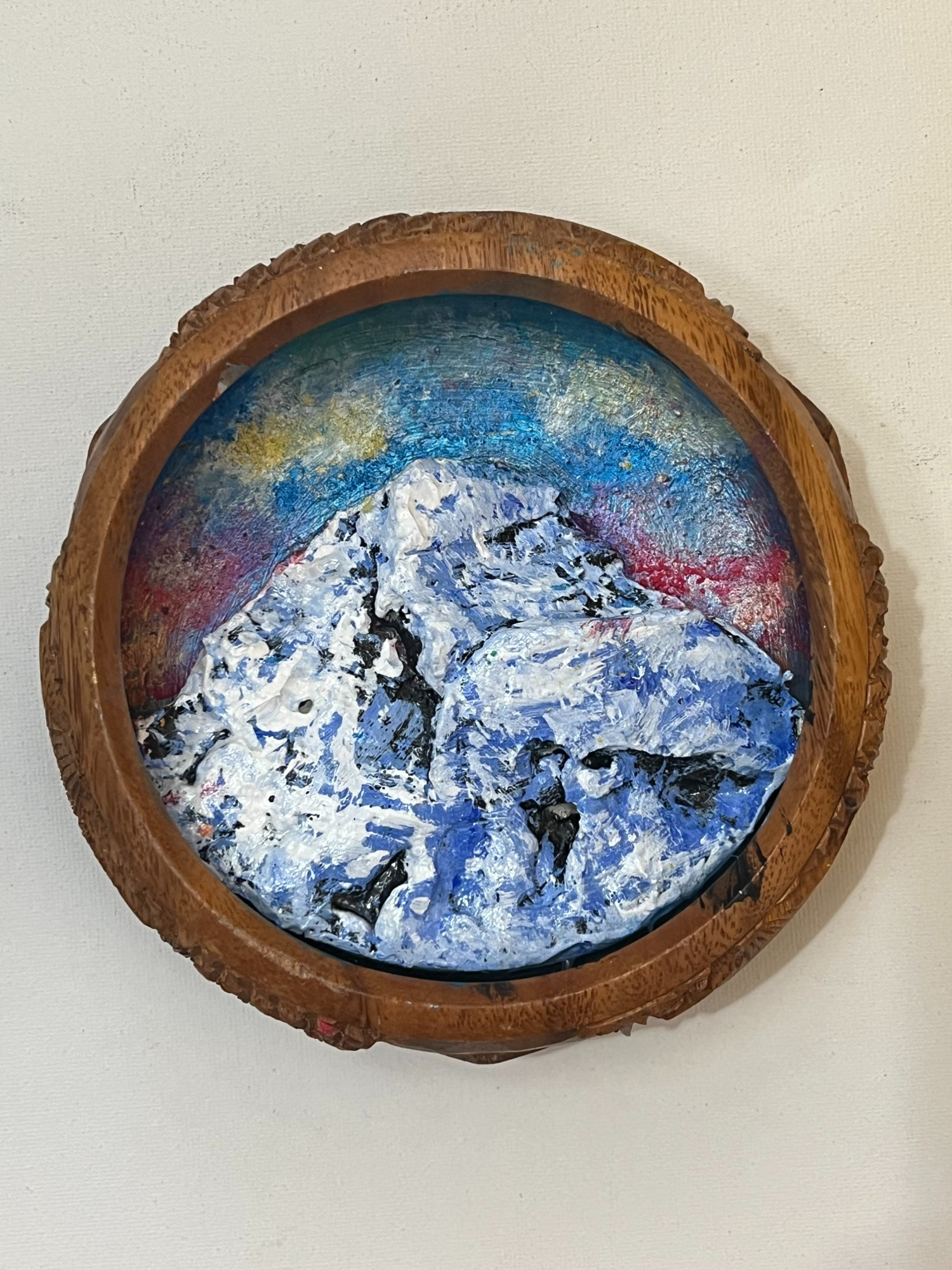 Carved wooden bowl with a painted sculpture of a snowy mountain against a colorful sky within.