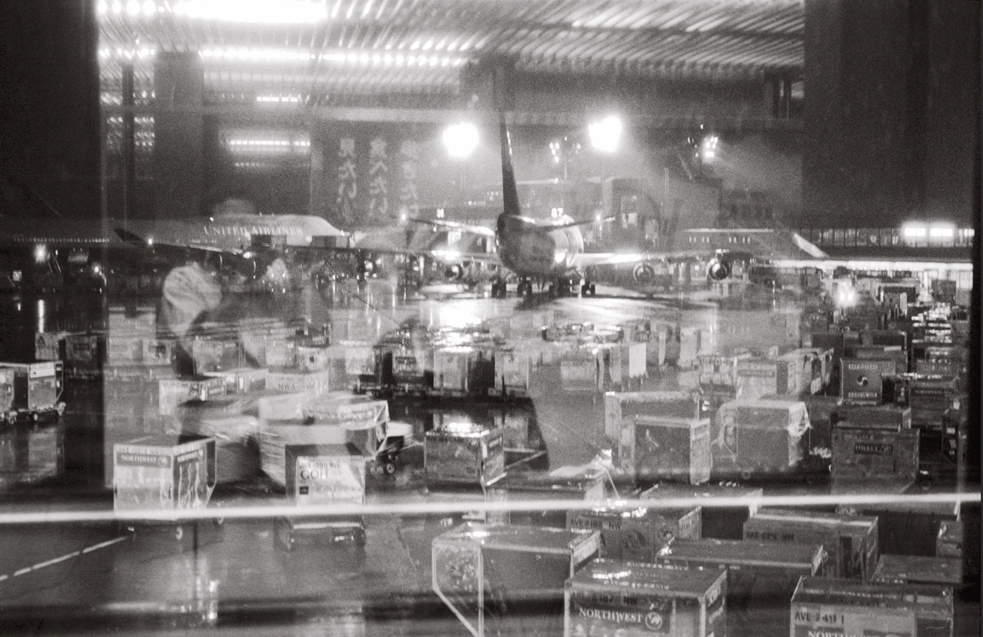 Photographed through an airport window, a Boeing 747 seen from behind is surrounded by dozens of luggage carts.