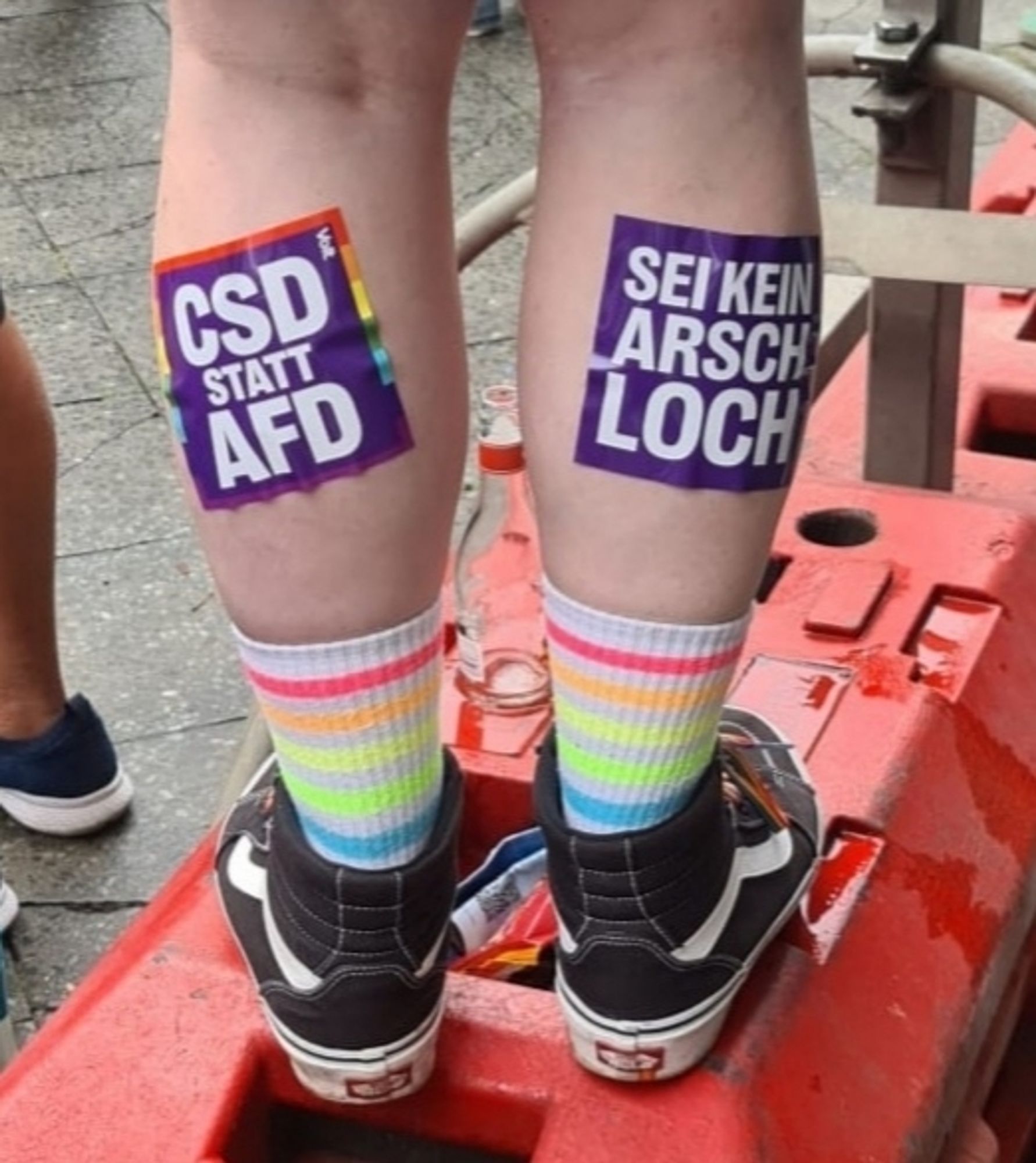 Meine Beine von hinten mit "CSD STATT AFD" und "SEI KEIN ARSCHLOCH" Stickern der Partei Volt versehen