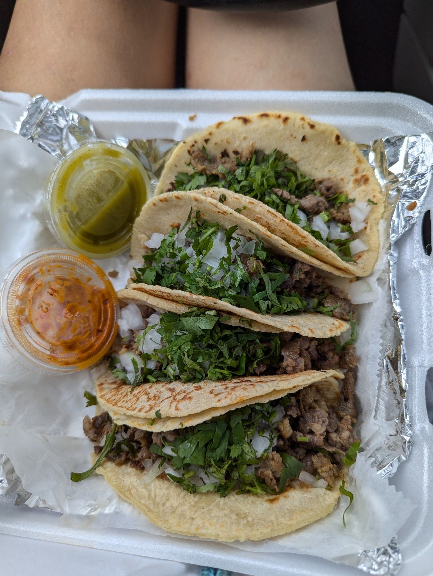 4 tacos in a Styrofoam container with red and green sauces