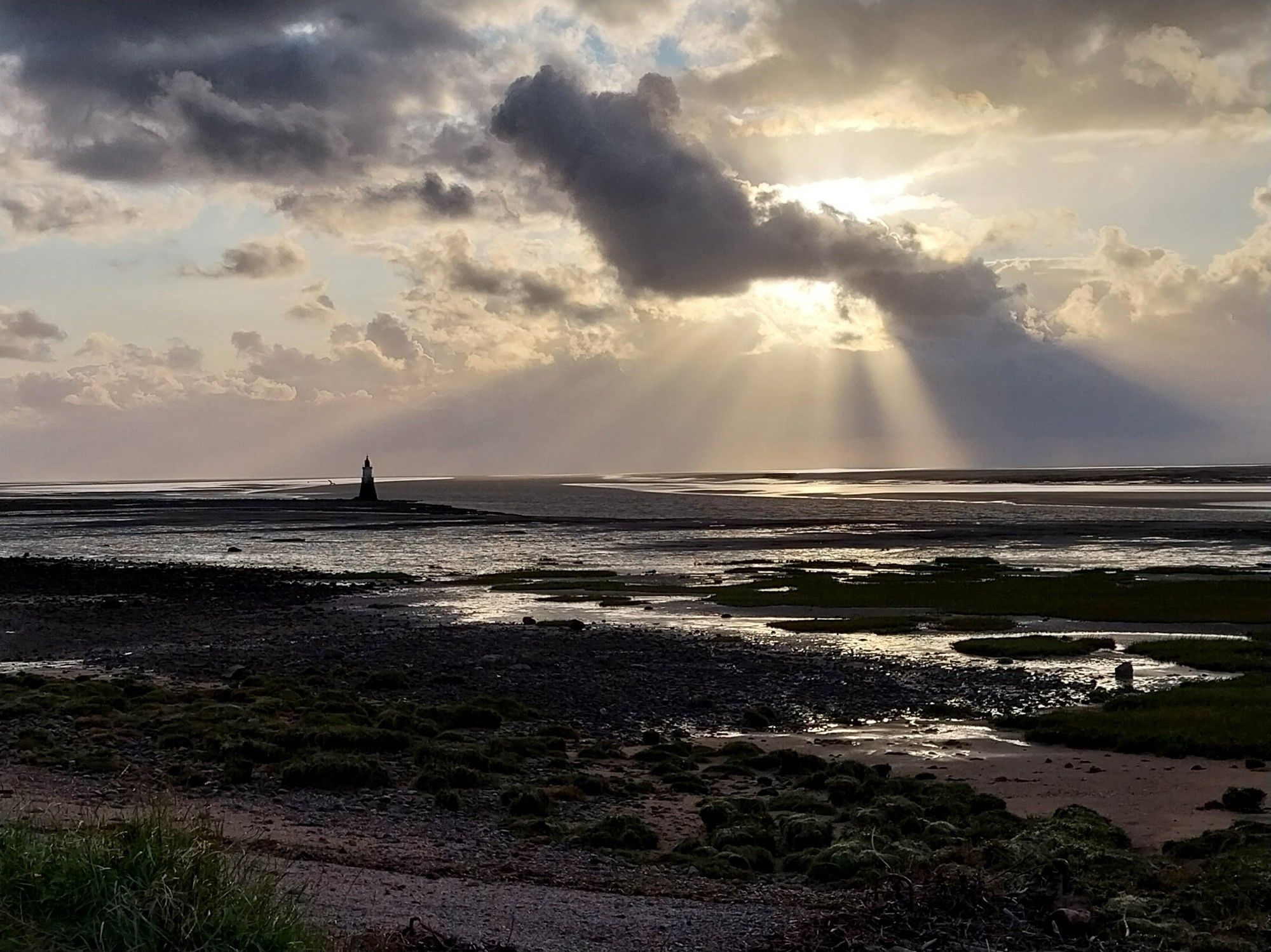 A coastal scene with sunbeams shining down on a lighthouse