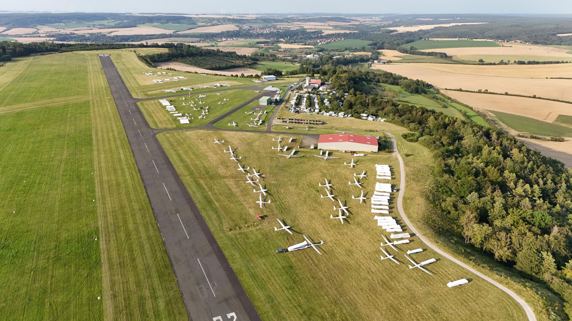 Flugplatz von oben. Die Landebahn ist leer. Am dem Platz alles voller Flugzeuge. Der Campingplatz ist ganz voll.