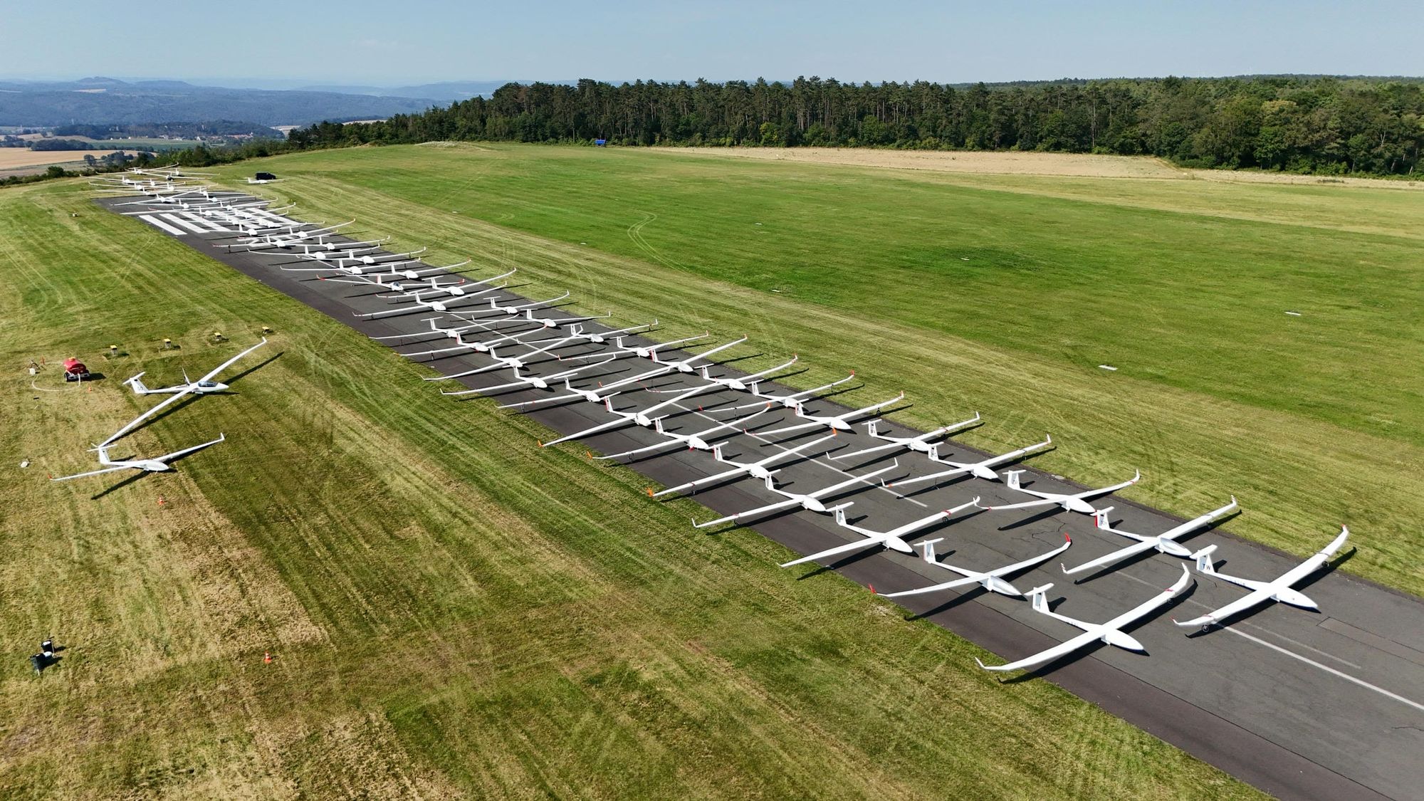 Luftbild: ganz viele Segelflugzeuge auf einer Asphaltstartbahn in Zweierreihe aufgebaut.