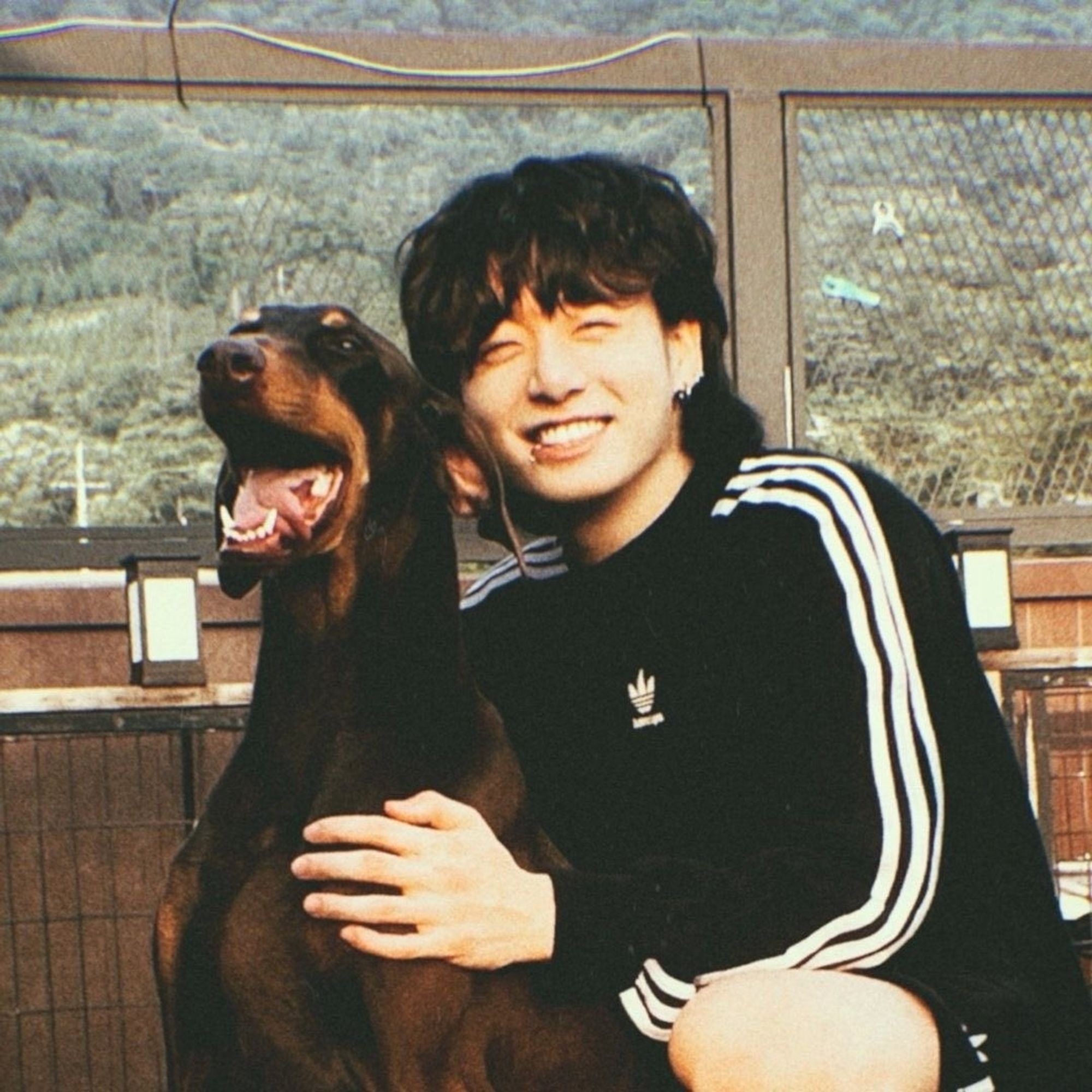 Jungkook of BTS smiling cutely while sitting down hugging his dog Bam