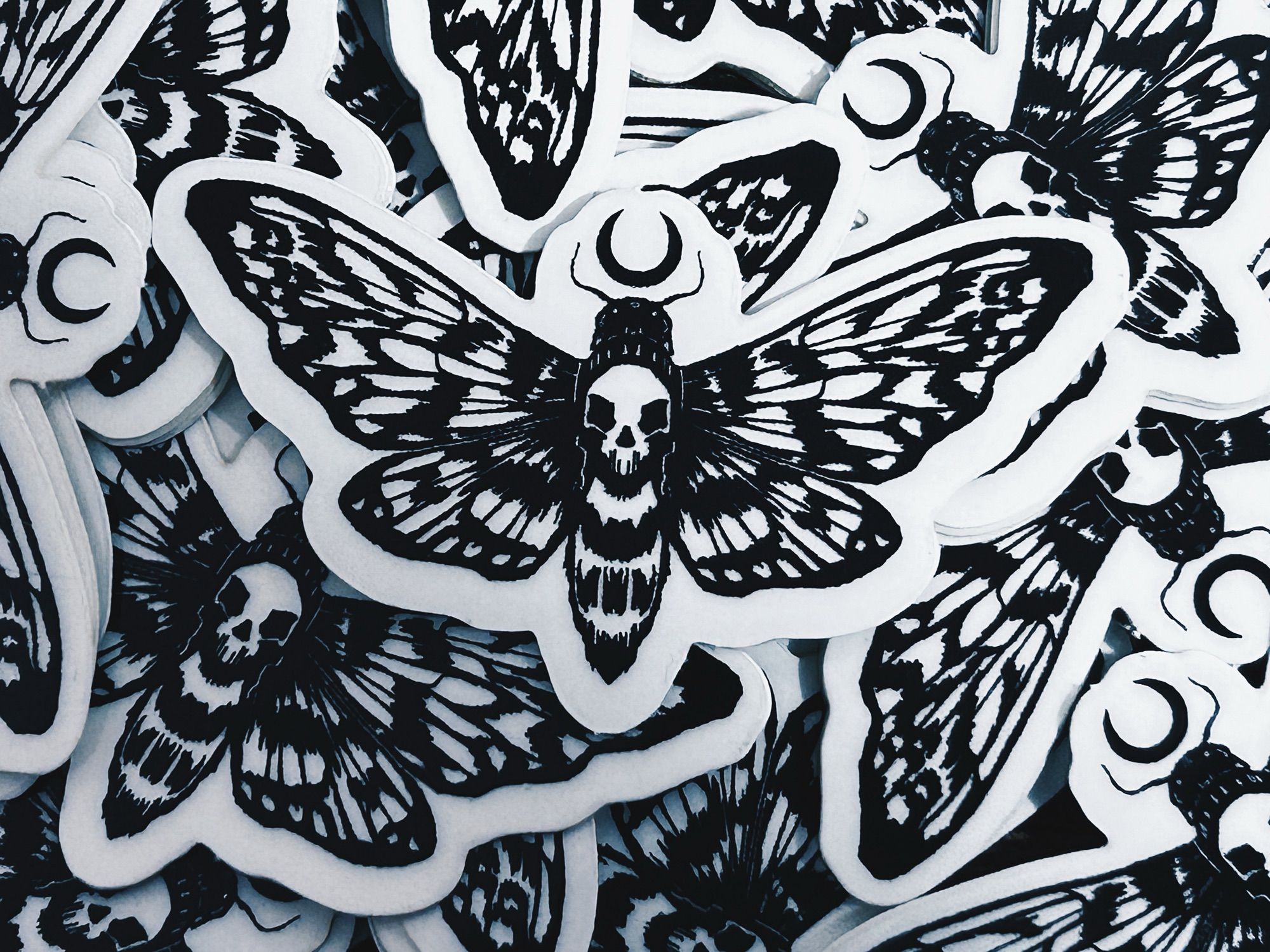 Pile of black death’s-head moth stickers with tiny crescent moons above their heads