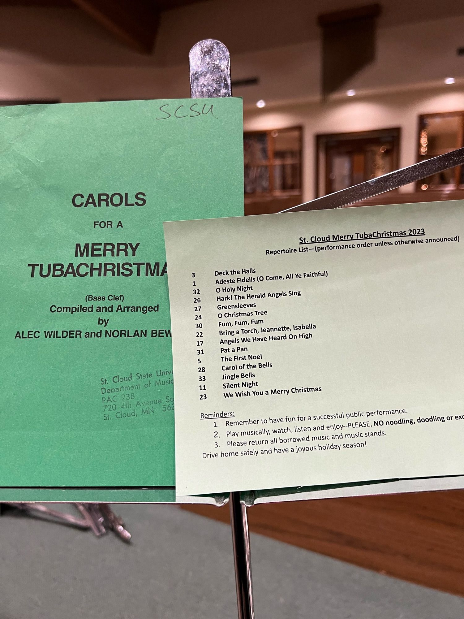 The Carols for a Merry TubaChristmas book with a set list on a wire music stand inside a church.