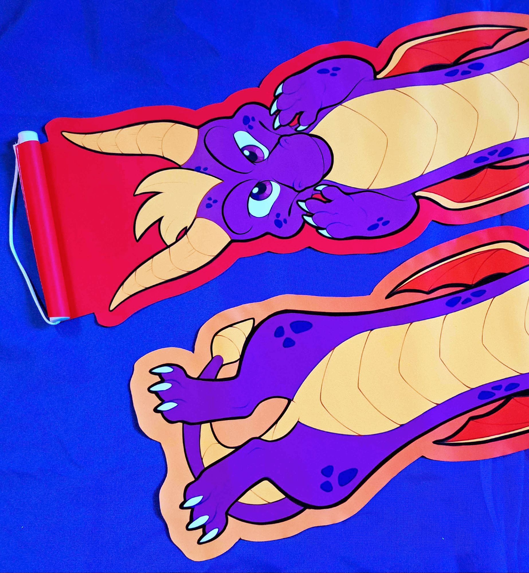 A photograph of a pin banner depicting an elongated Spyro the dragon (two of them laid at opposite ends side by side to fit in the frame).