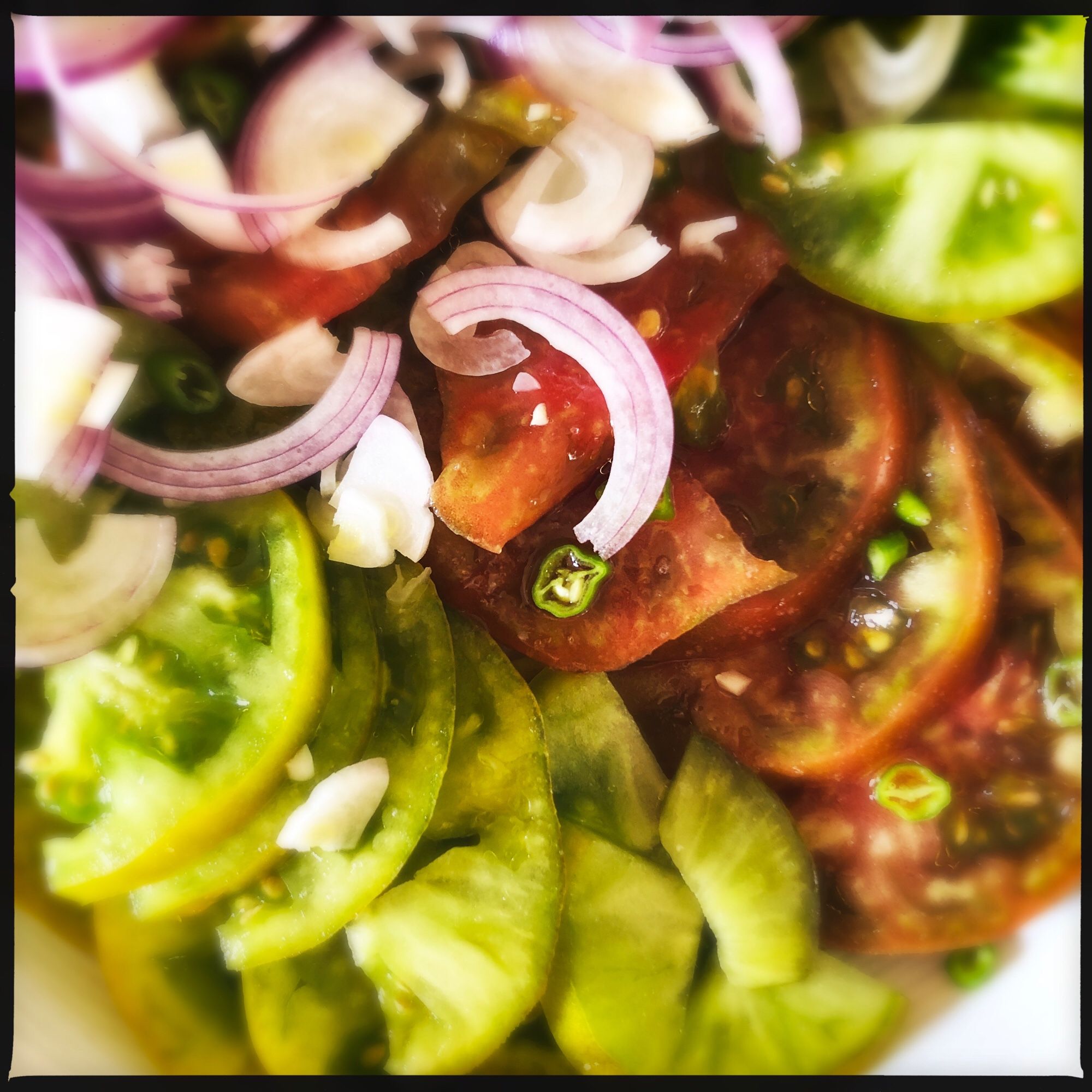 Ein Tomatensalat aus grünen Tomaten und einer „rot schwarzen“, rote Zwiebel und grüne Peperoni.