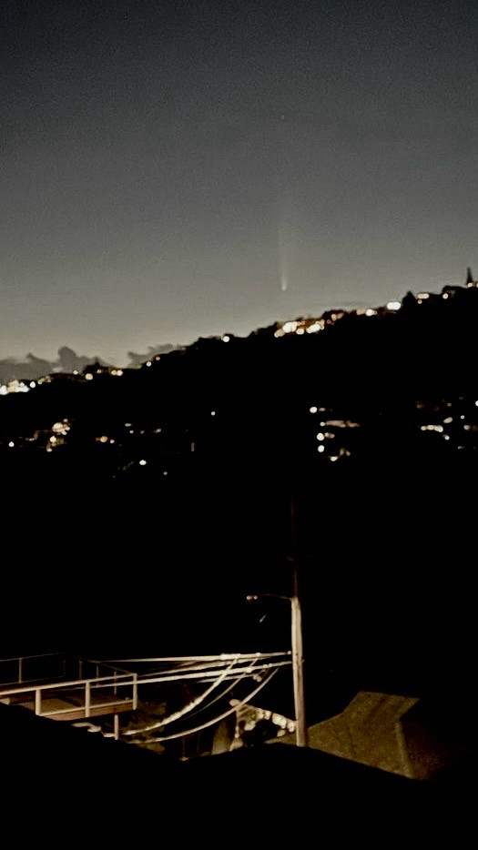 Comet Tschuchinshan-ATLAS descending behind a mountain ridge in the night sky over Honolulu. 