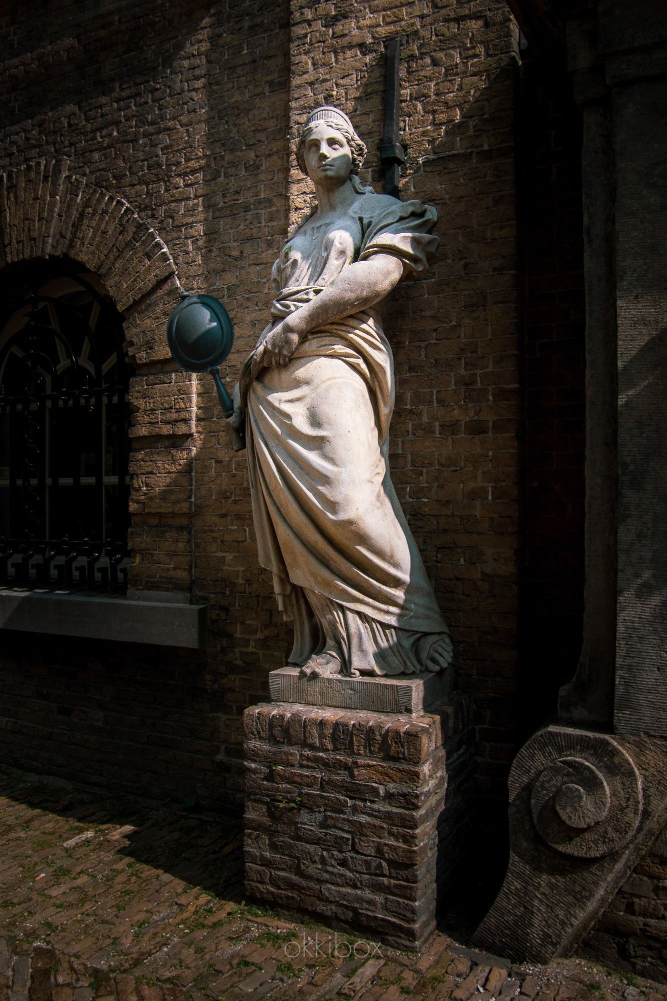 Op deze foto zie je vrouwe Wijsheid in het zonnetje met een spiegel in haar hand. 

De beelden Wijsheid en Standvastigheid ter weerszijden van het wapen van Gouda staan in museumtuin Gouda. De beelden uit 1695 van kunstenaar Jan Gijselingh jr. zijn afkomstig uit een nis aan de voorzijde van het oude Goudse Stadhuis en moesten wijken voor de bouw van nieuwe ramen. 