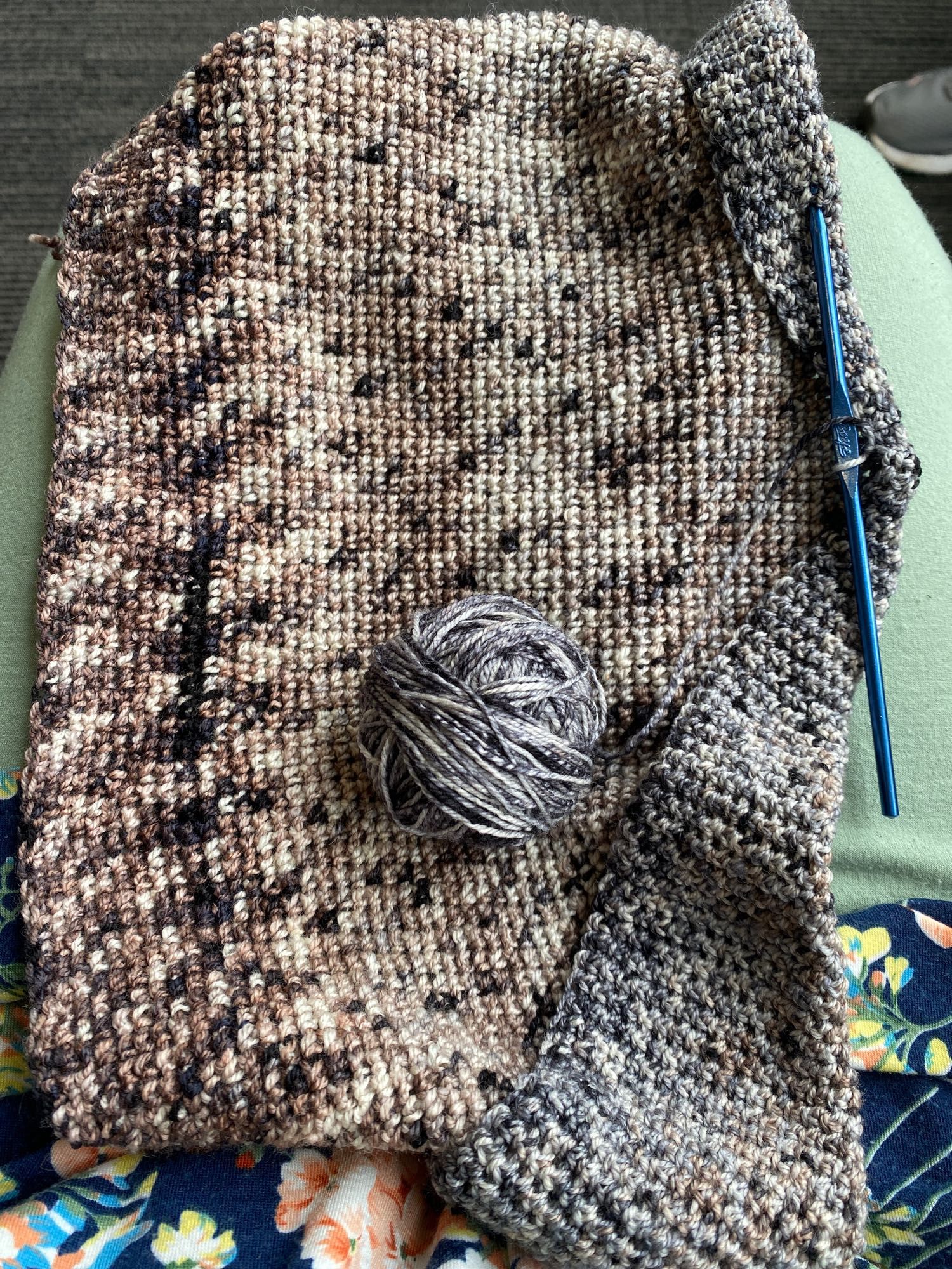 Tan, grey, and brown varigated yarn mostly used up, with a blue crochet hook on the right side, on my lap.