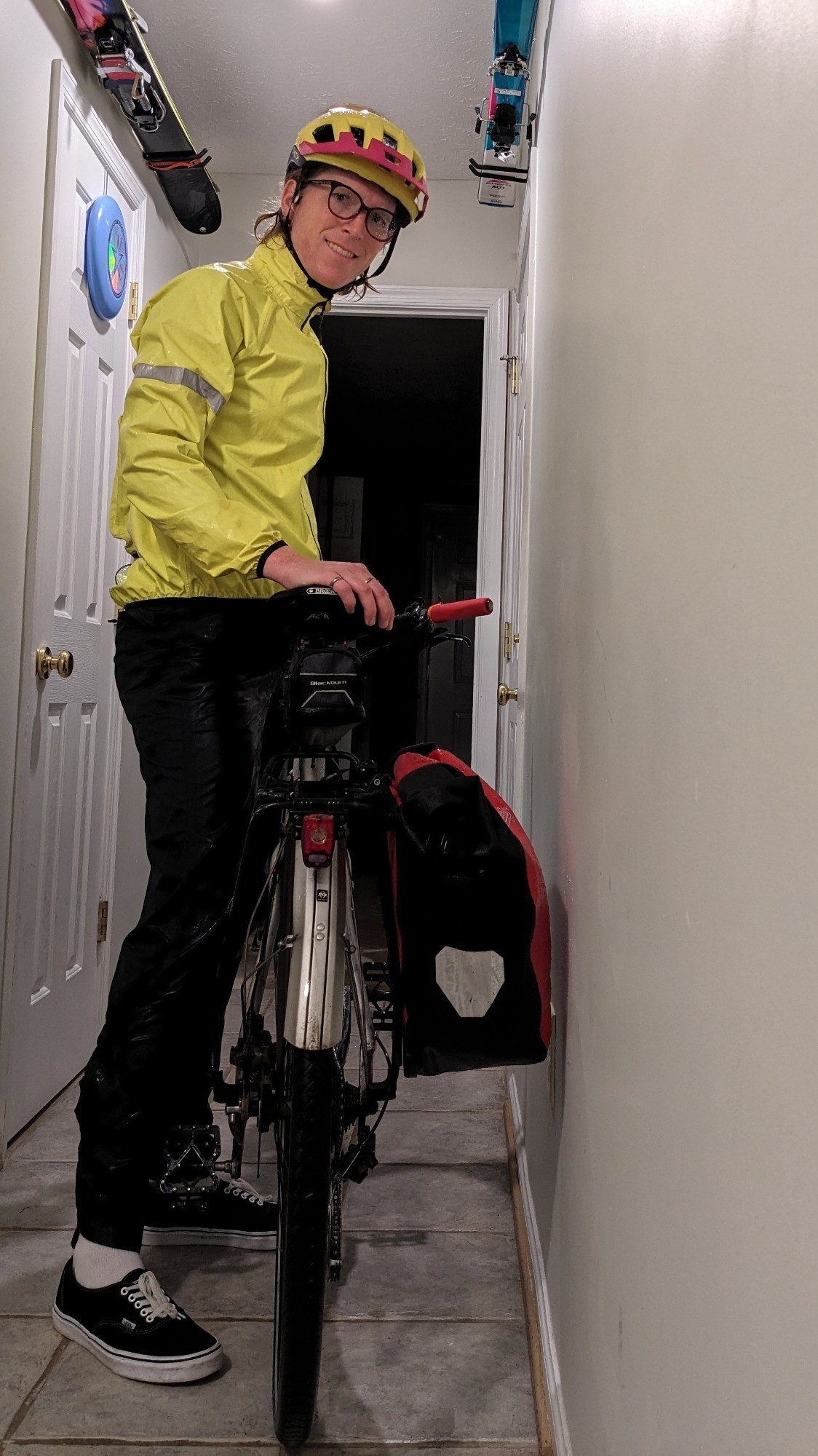 a tall aquamarine and blonde haired lass wearing a full rainsuit standing next to her bichael with waterproof pannier and full fenders, both she and her bichael are dripping loads of water in her front hallway