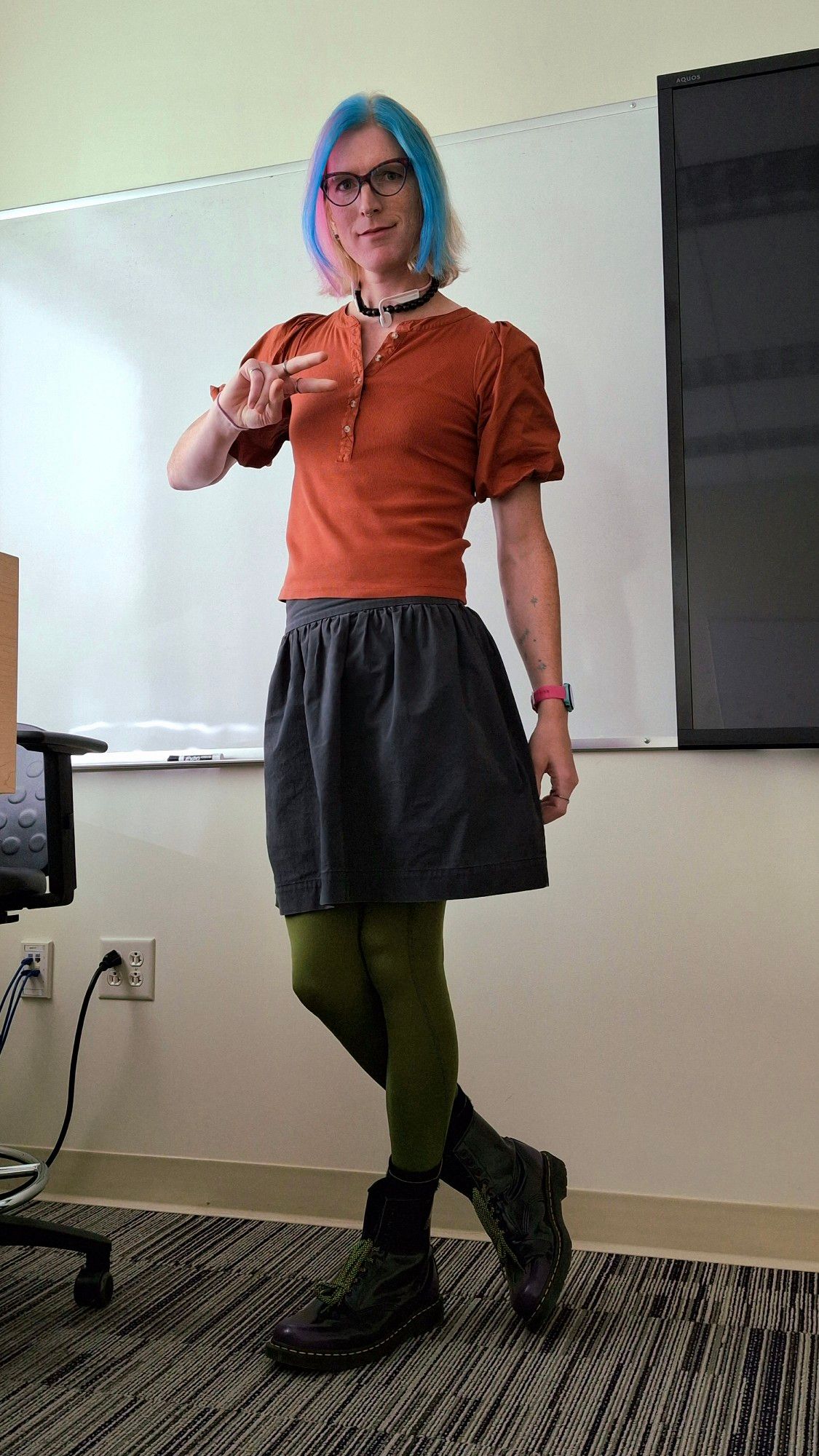 Tilda wearing a burnt orange puff sleeve Henley top with a poofy anthracite flared midi skirt and olive green leggings with black and purple docs marten to offset her aqua and pink and blonde hair. she is the embodiment of fall today.