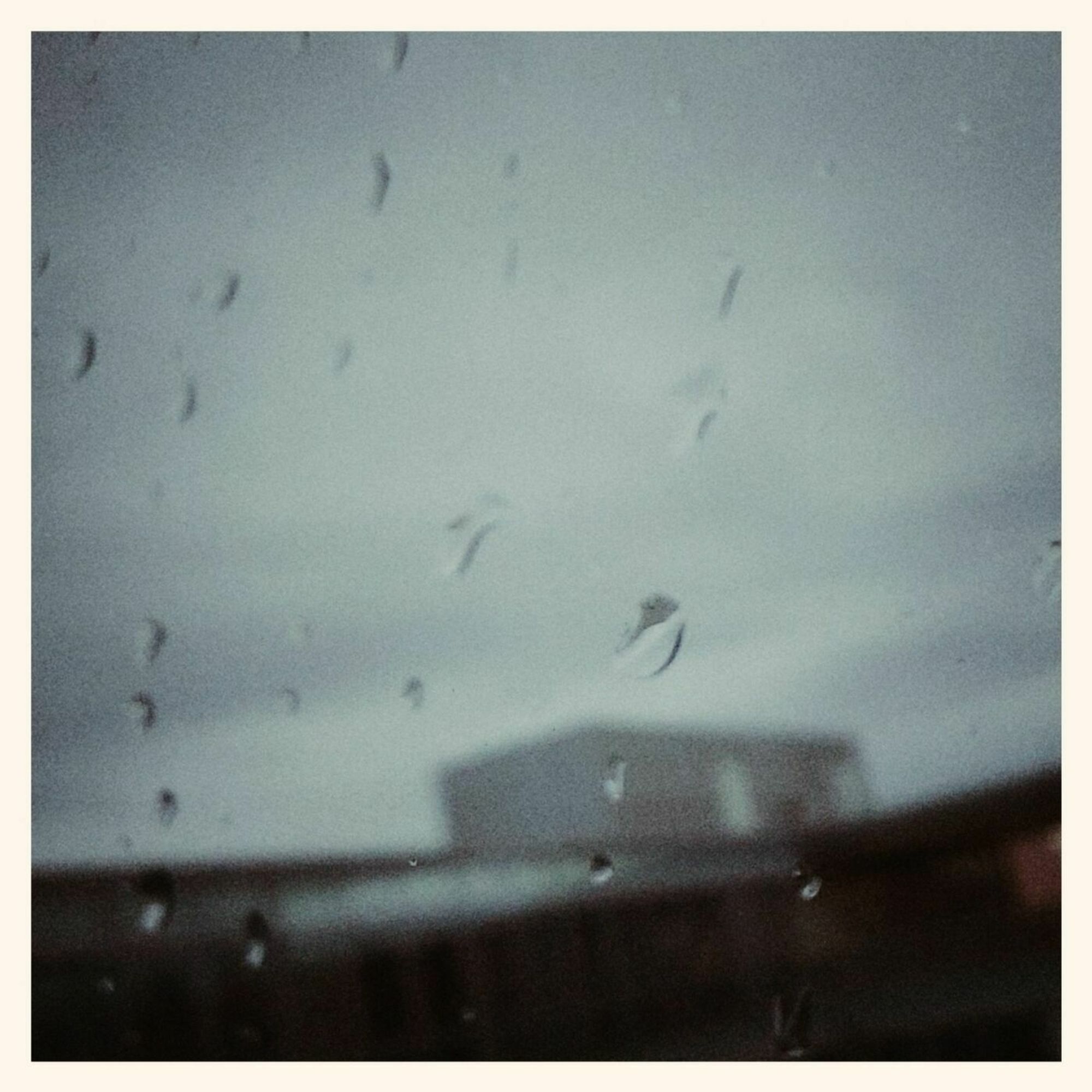 Grey sky, concrete facade and raindrops on a windowpane in front.