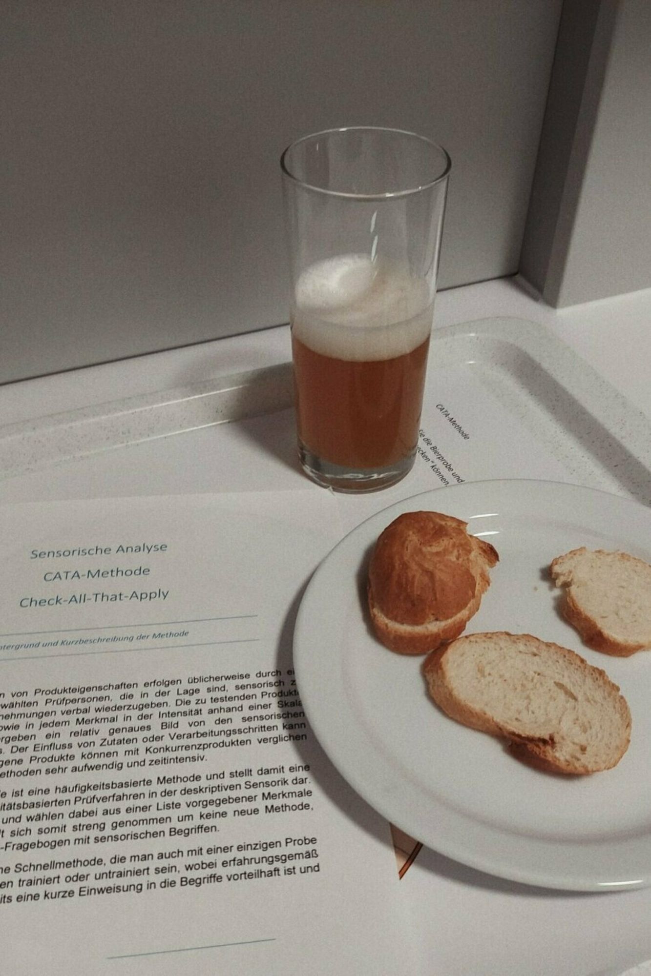 Ein Glas mit Bier, ein Teller mit Weißbrot und ein Formular zur Versuchsanordnung Sensorische Anslyse.