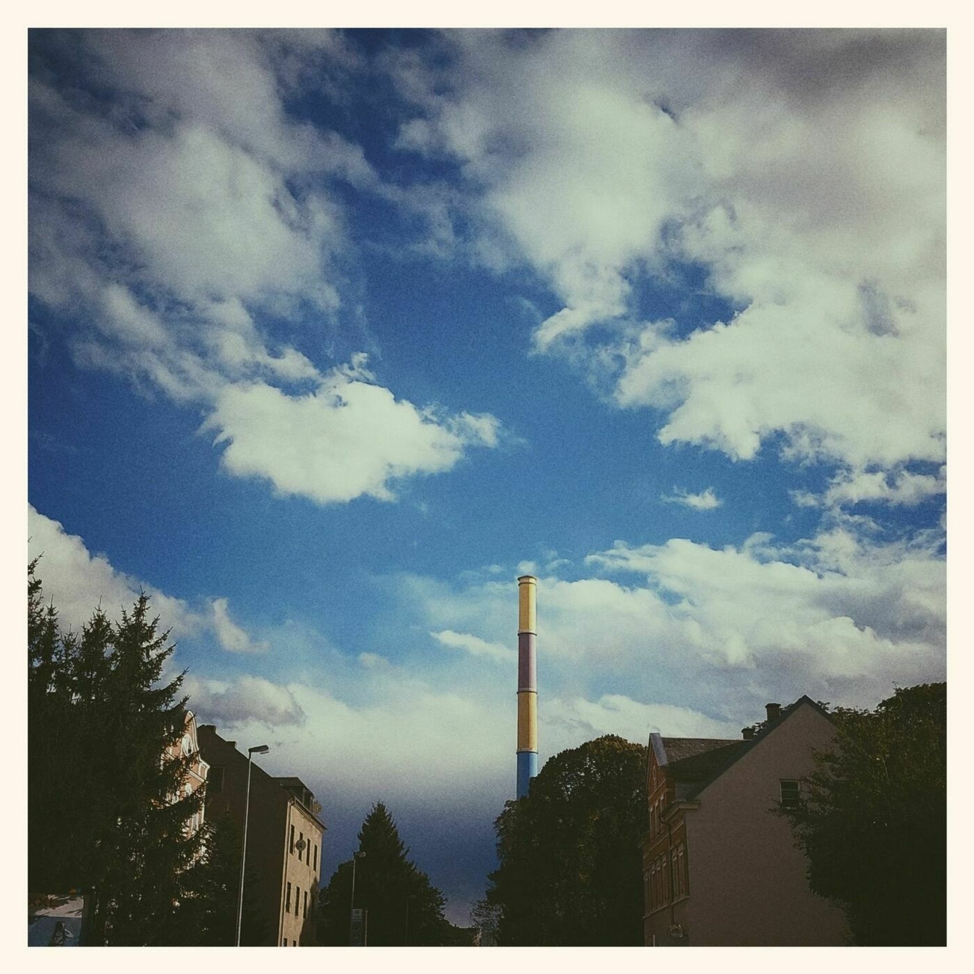 Wild clouds, blue sky, old buildings and a coloured chimney. 