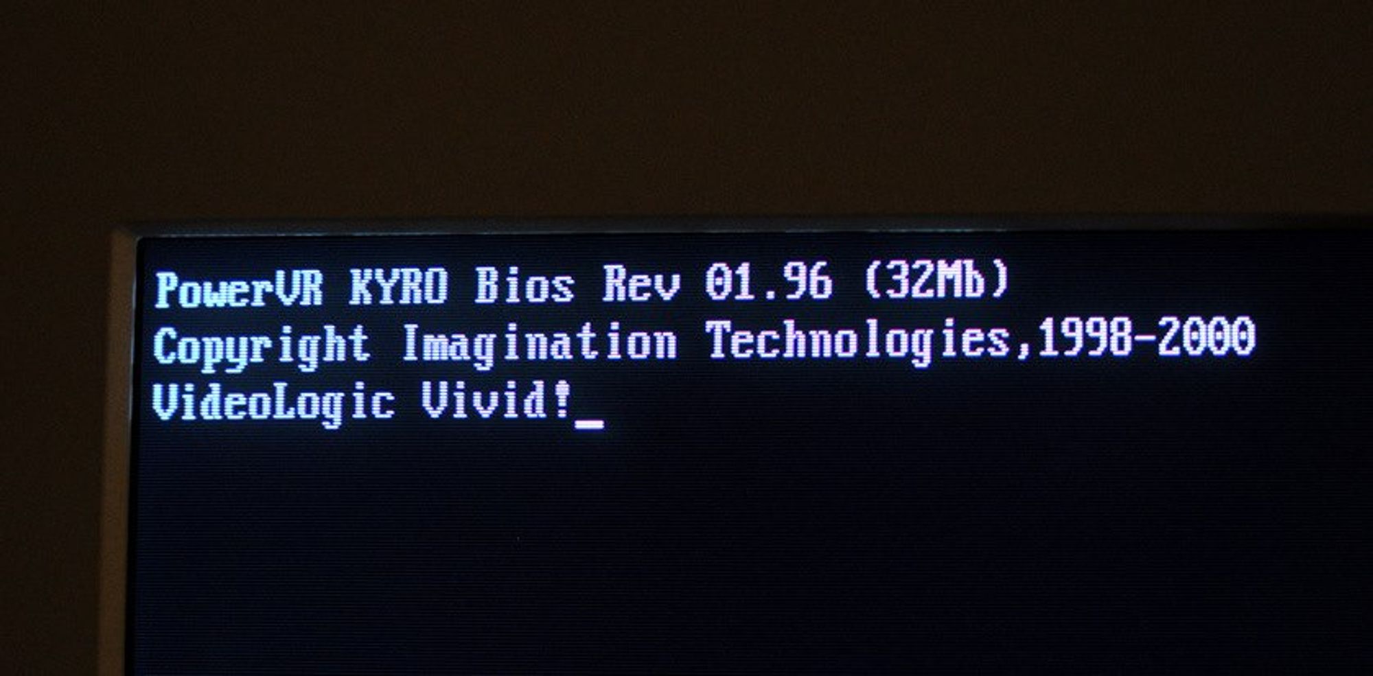 Foto eines Computer-Röhrenmonitors beim Rechner-Start. In unscharfer, heller Schrift auf dunklem Hintergrund ist dort zu lesen:

PowerVR KYRO Bios Rev 01.96 (32 Mb)
Copyright Imagination Technologies, 1998-2000
Videologic Vivid!